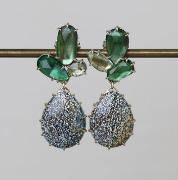 Pair of earrings with green gemstones and textured silver drops on a gray background
