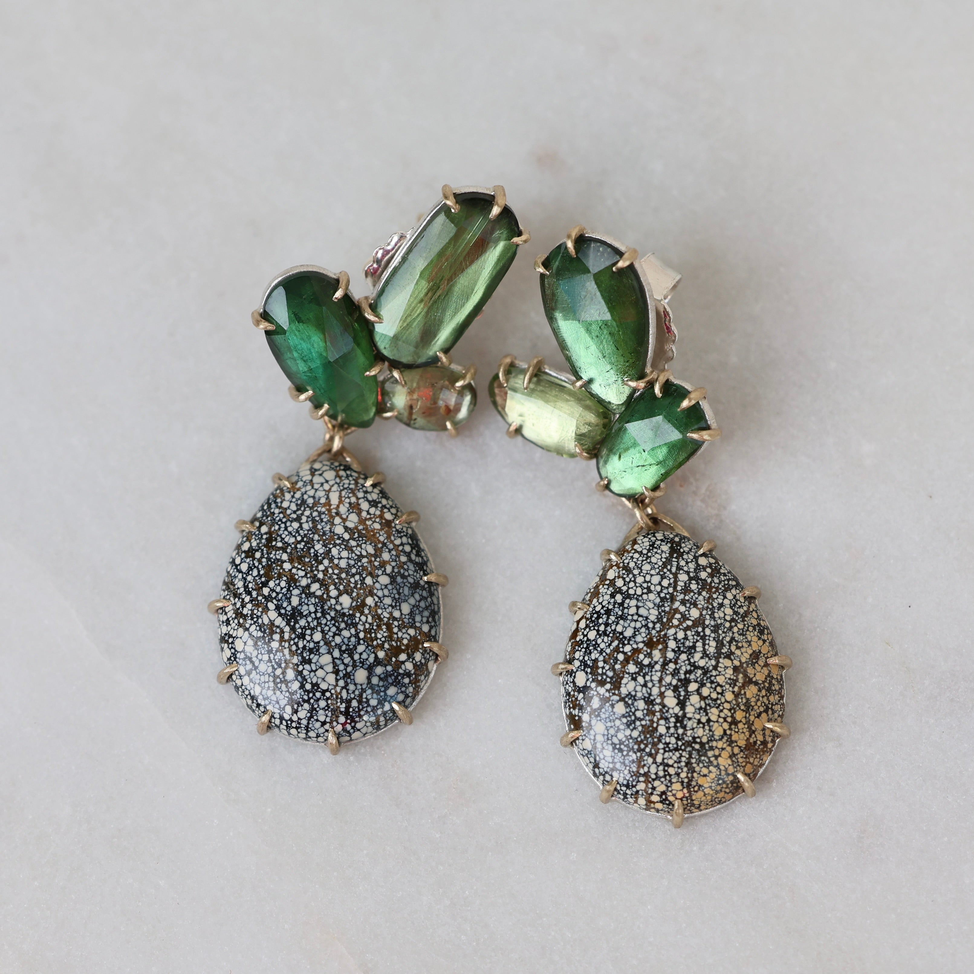 Pair of earrings with green and gray stones on a light background