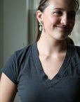 woman wearing dark grey shirt with green earrings