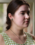 Woman wearing a green checkered dress and green tourmaline studs with a blurred background