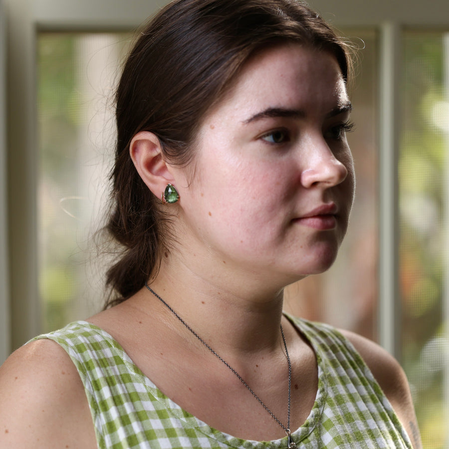 Woman wearing a green checkered dress and green tourmaline studs with a blurred background