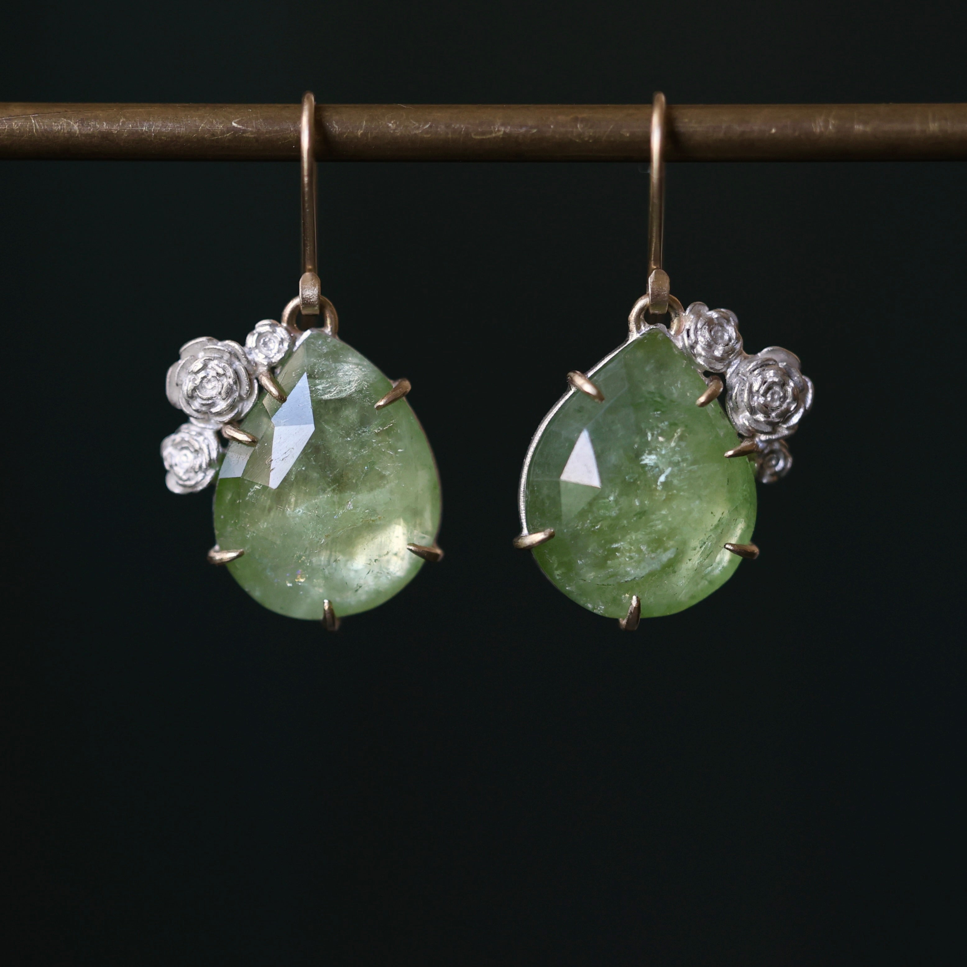 Bright green Tourmaline earrings with 14k yellow gold prongs and ear wires and bright sterling silver rose accents and stone seats on a dark green background.