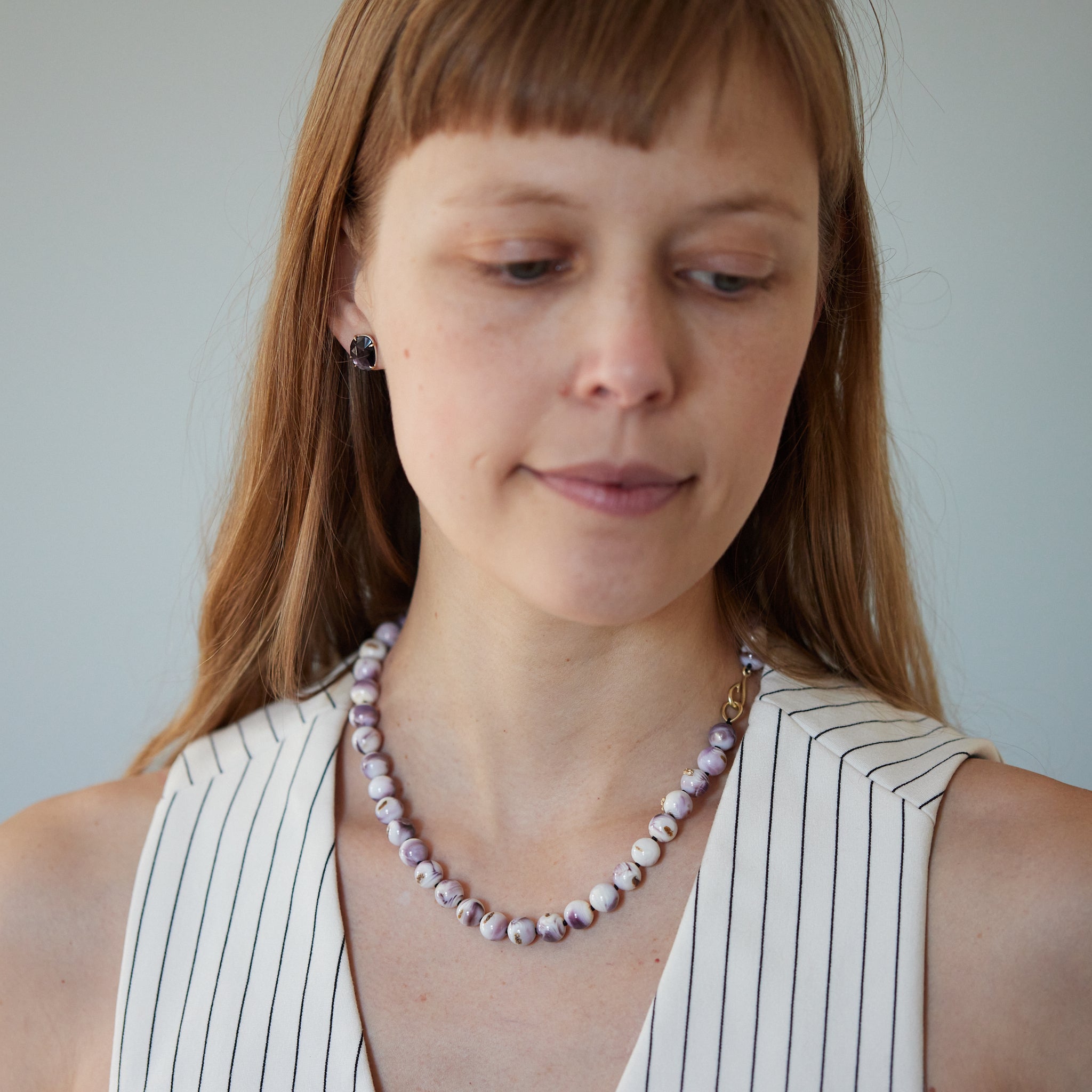 purple and white swirly beads of round quahog shells are strung on black silk and have gold barnacles attached throughout. A gold fish hook clasp attached the strand. Photographed on person.
