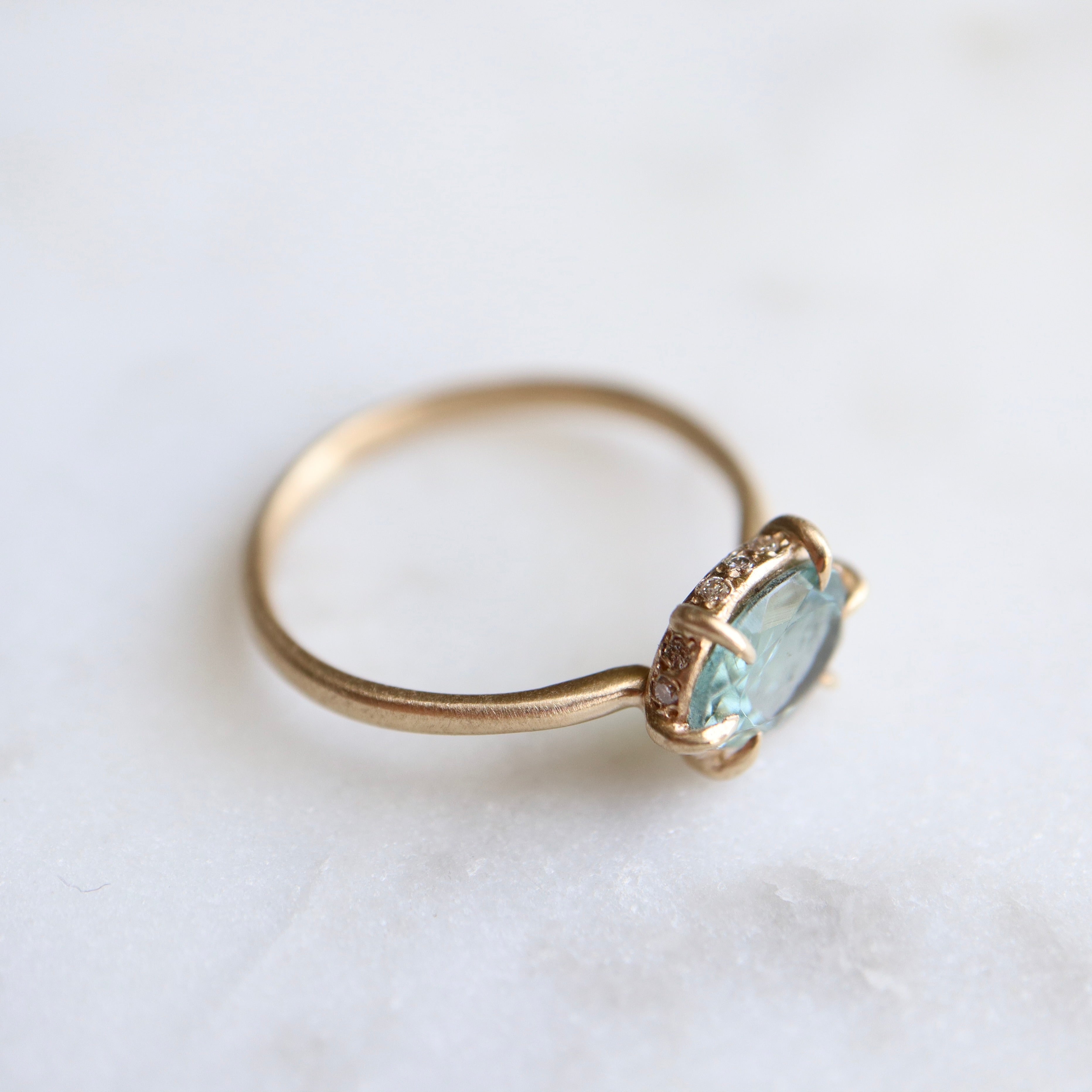 teal oval tourmaline stone set in a gold ring with gold prongs and diamonds set around the seat. side view.