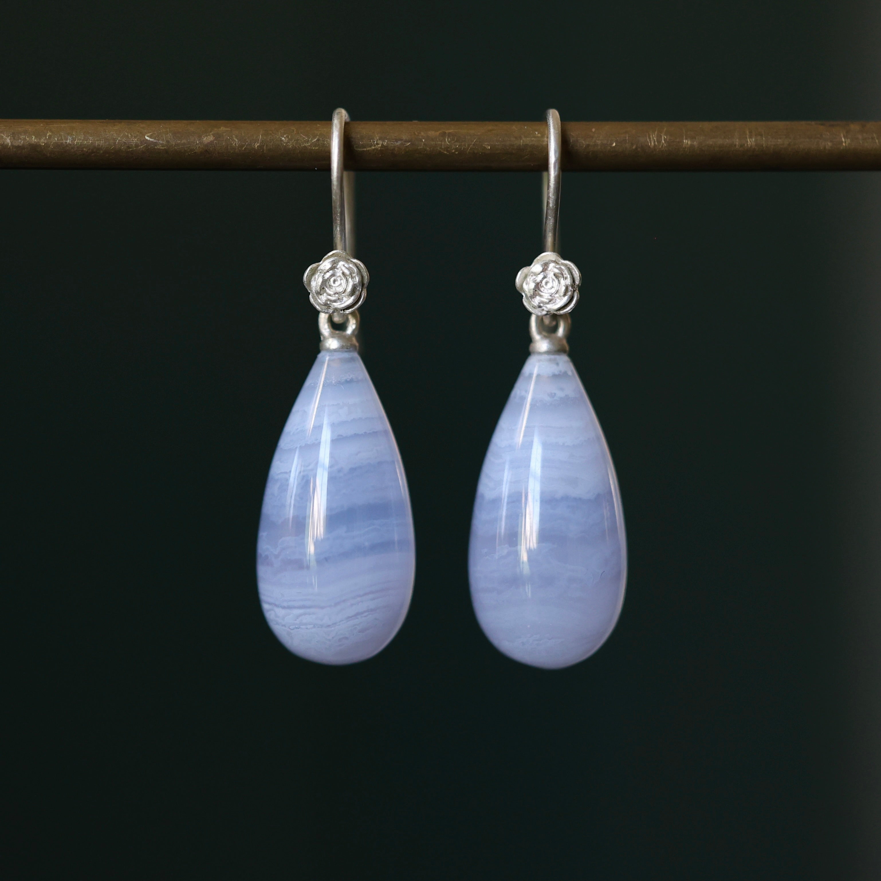 Lace Agate teardrop shaped earrings with bright sterling silver ear wires and rose accents on a dark green background. 