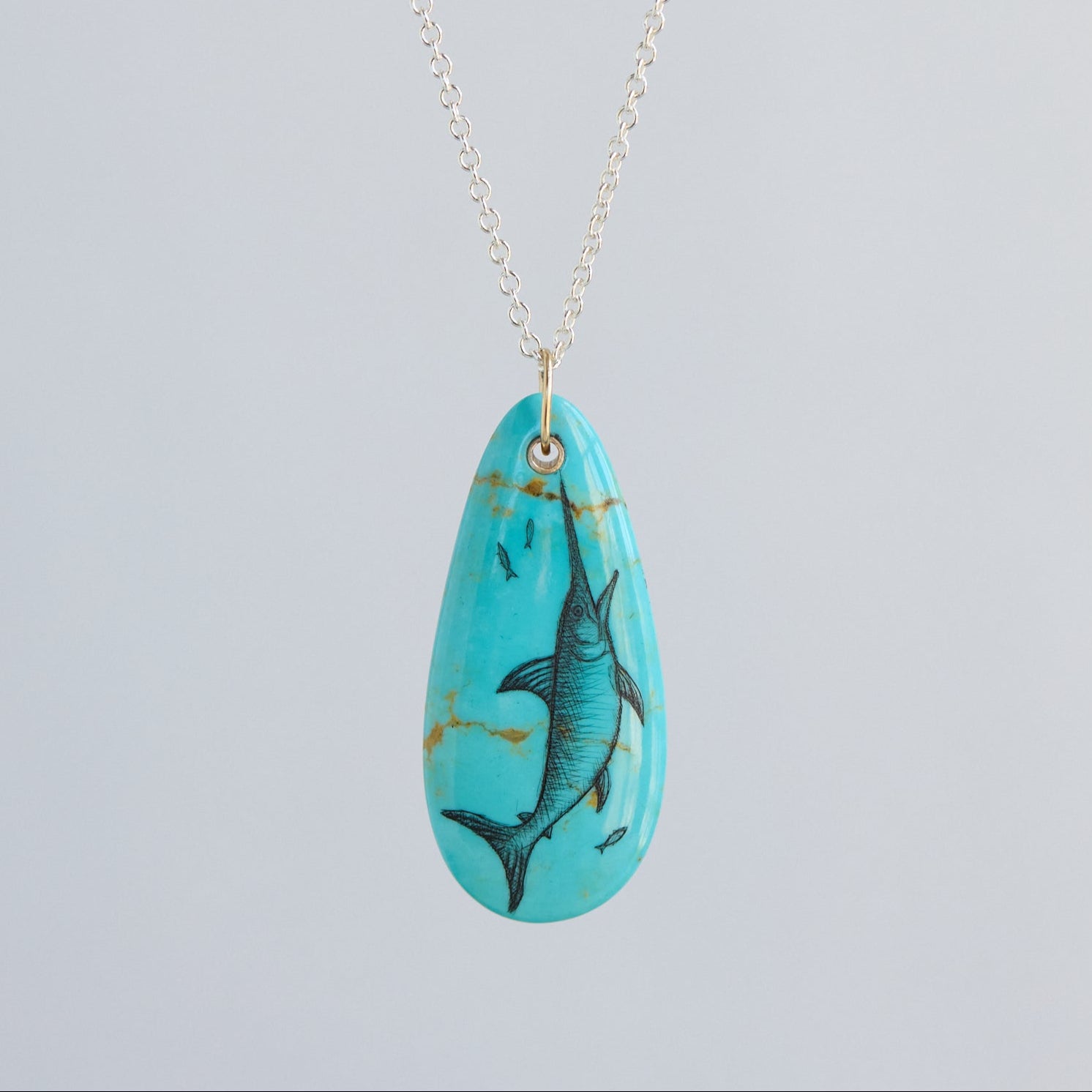 Turquoise pendant with fish design on a silver chain against a light gray background