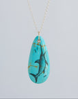 Turquoise pendant with fish design on a silver chain against a light gray background
