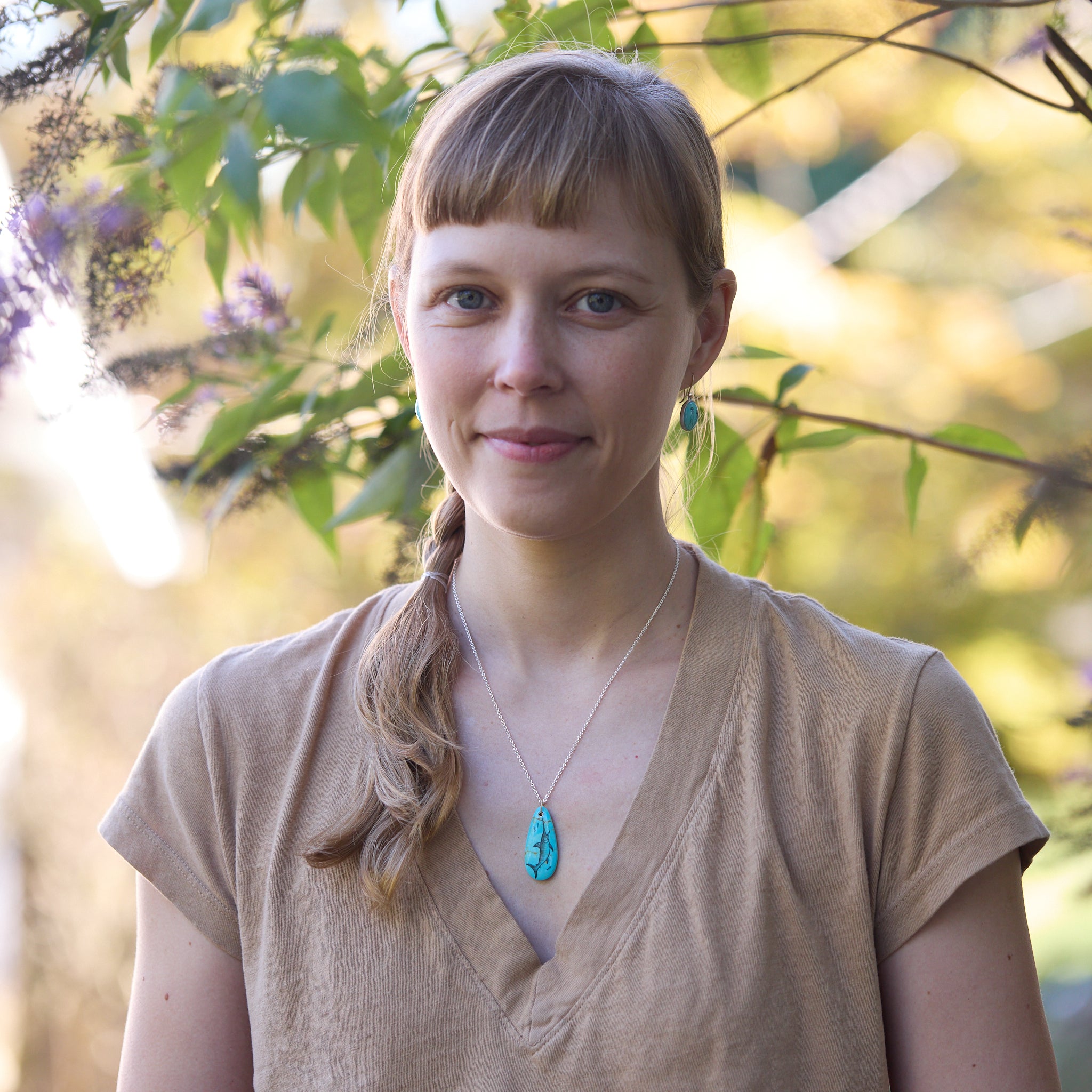 Woman with a braid and turquoise necklace and earrings standing in front of green foliage