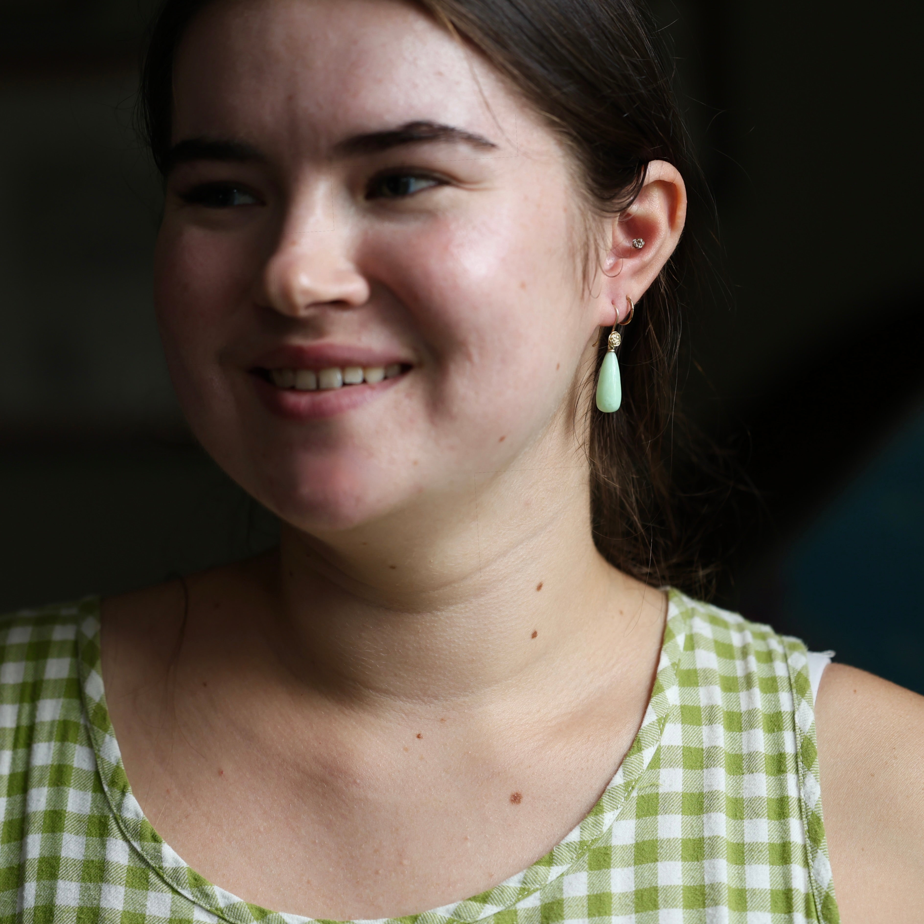 Woman wearing a green checkered dress and green drop earrings with a blurred dark background