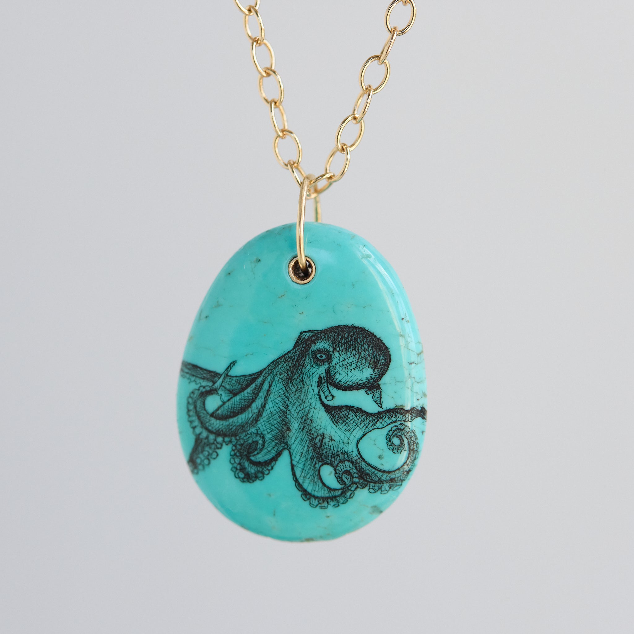 Turquoise pendant with octopus design on a gold chain against a light gray background