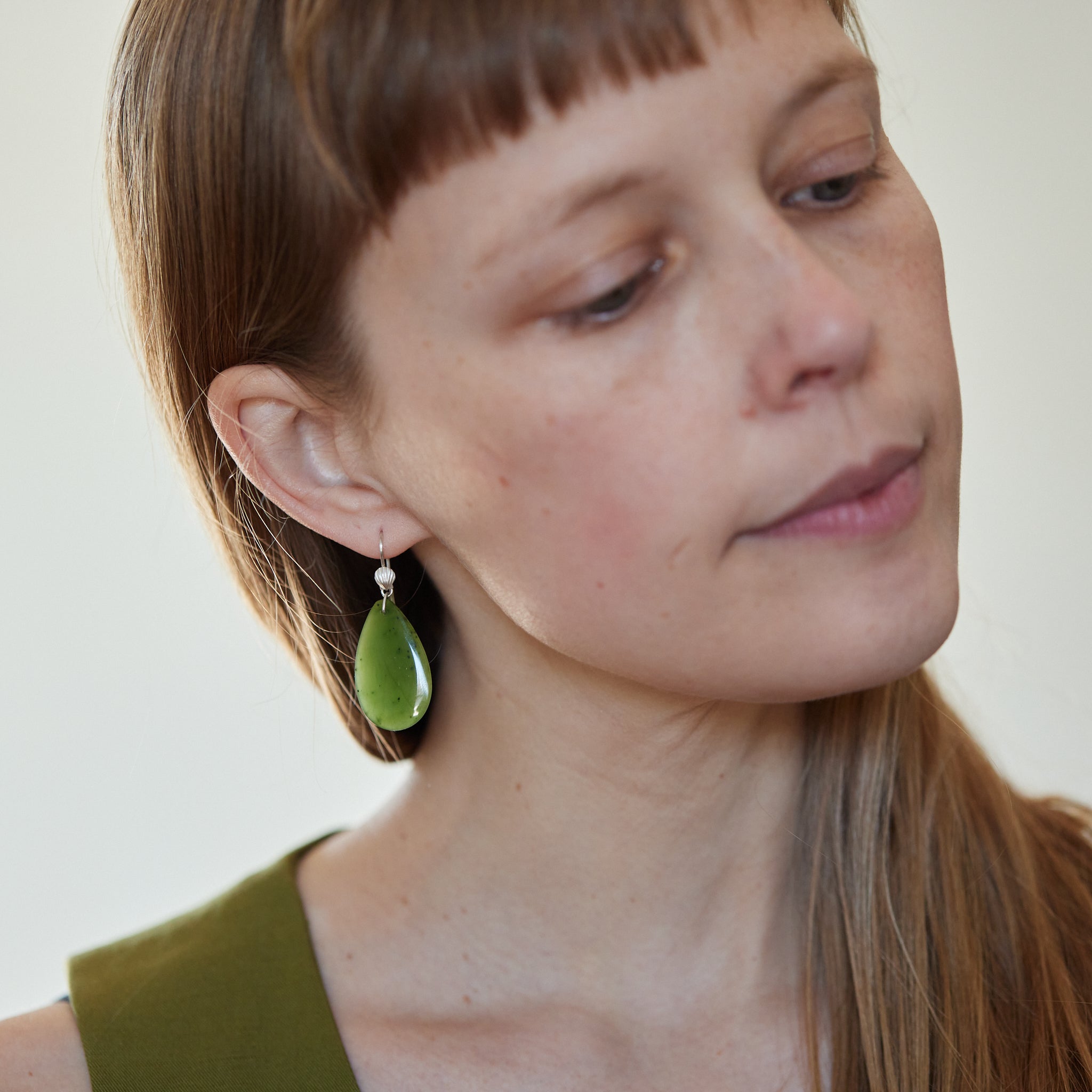 green teardrops under silver scallop ear wires. Photographed on person.