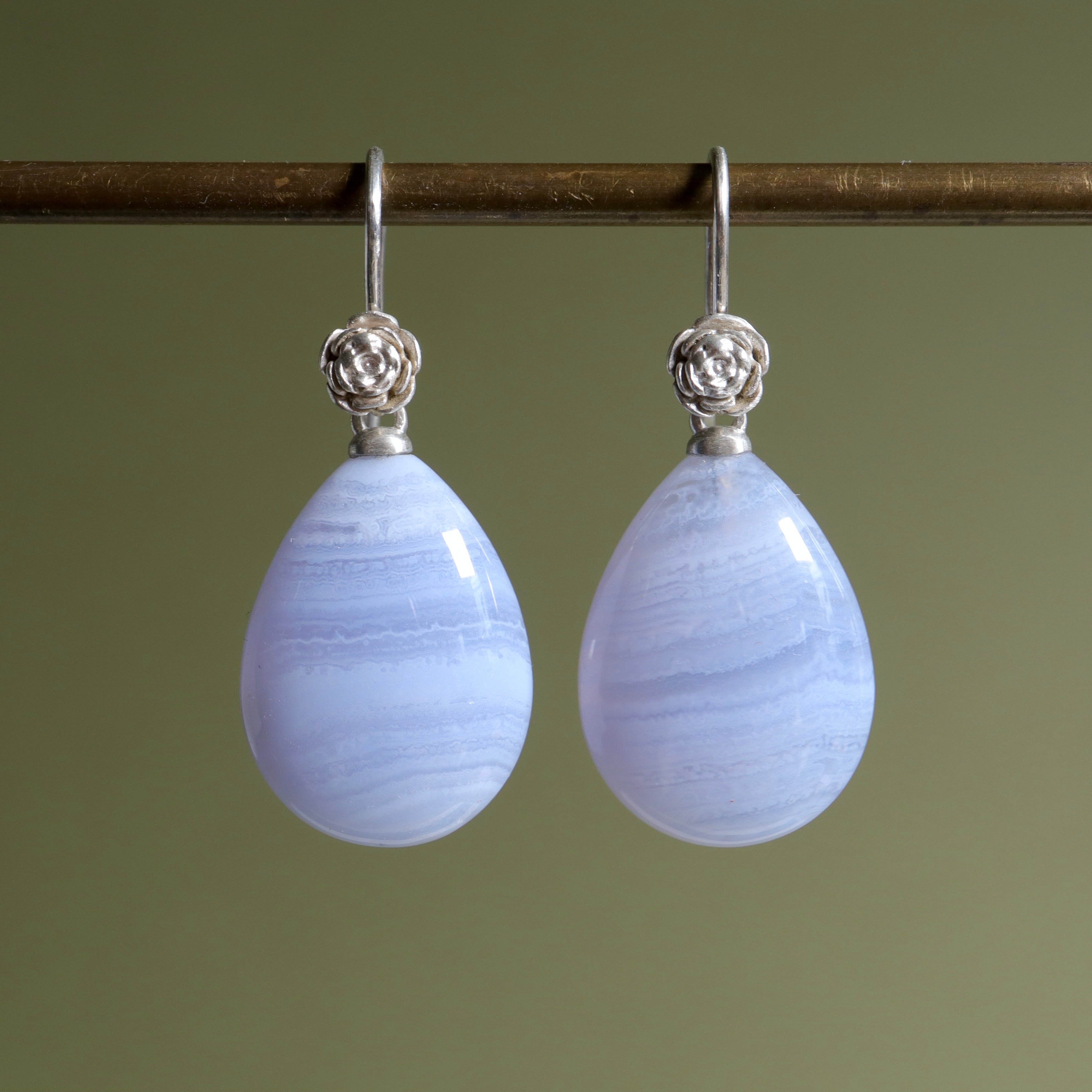 swirly pale blue lace agate teardrops hang beneath silver ear wires featuring little silver roses on them