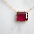 pink rectangular stone with in gold prongs on a gold chain with diamonds set in a hidden halo on the side of the setting. photographed on white marble.