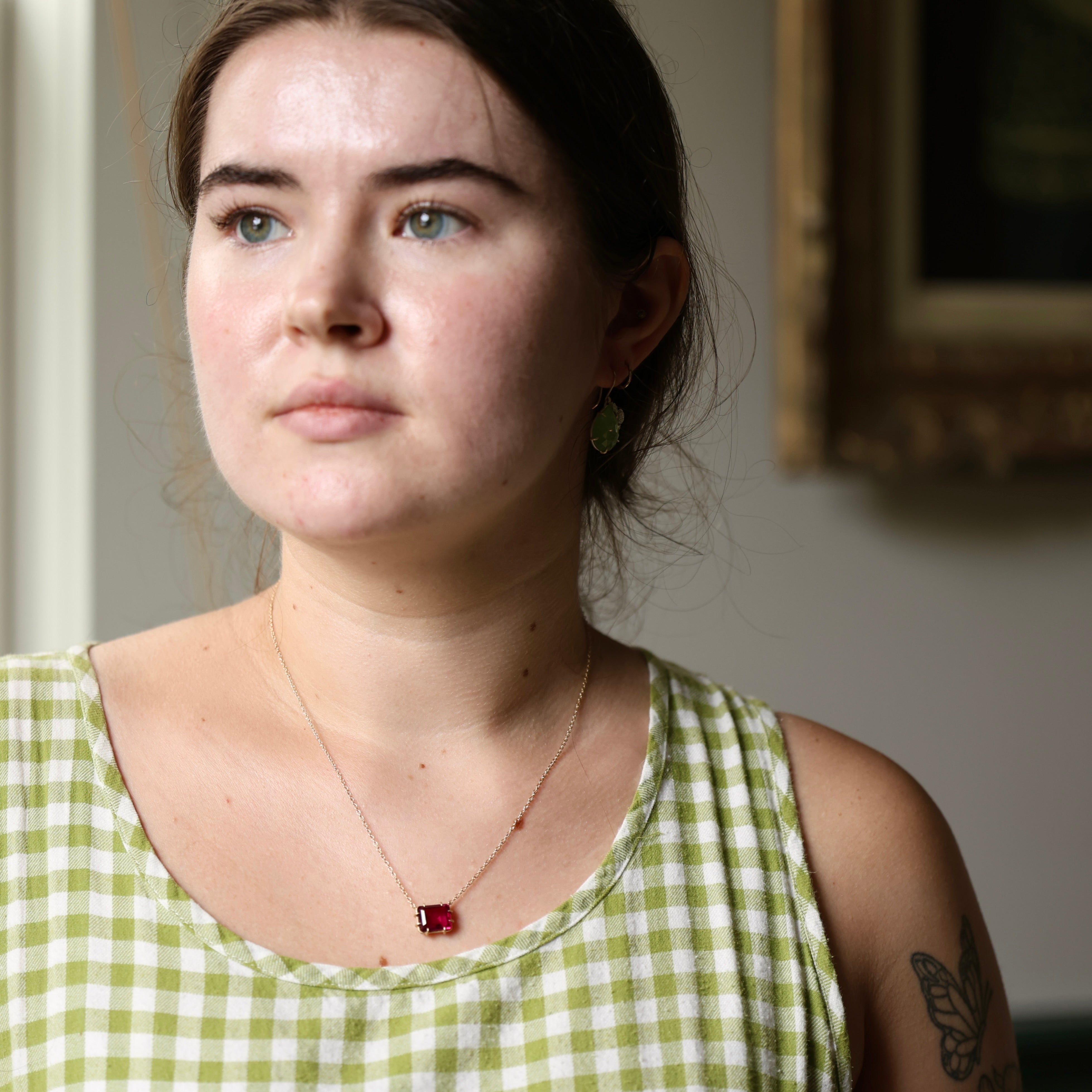 Woman wearing a green checkered dress with a red pendant necklace, standing indoors.