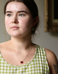 Woman wearing a green checkered dress with a red pendant necklace, standing indoors.