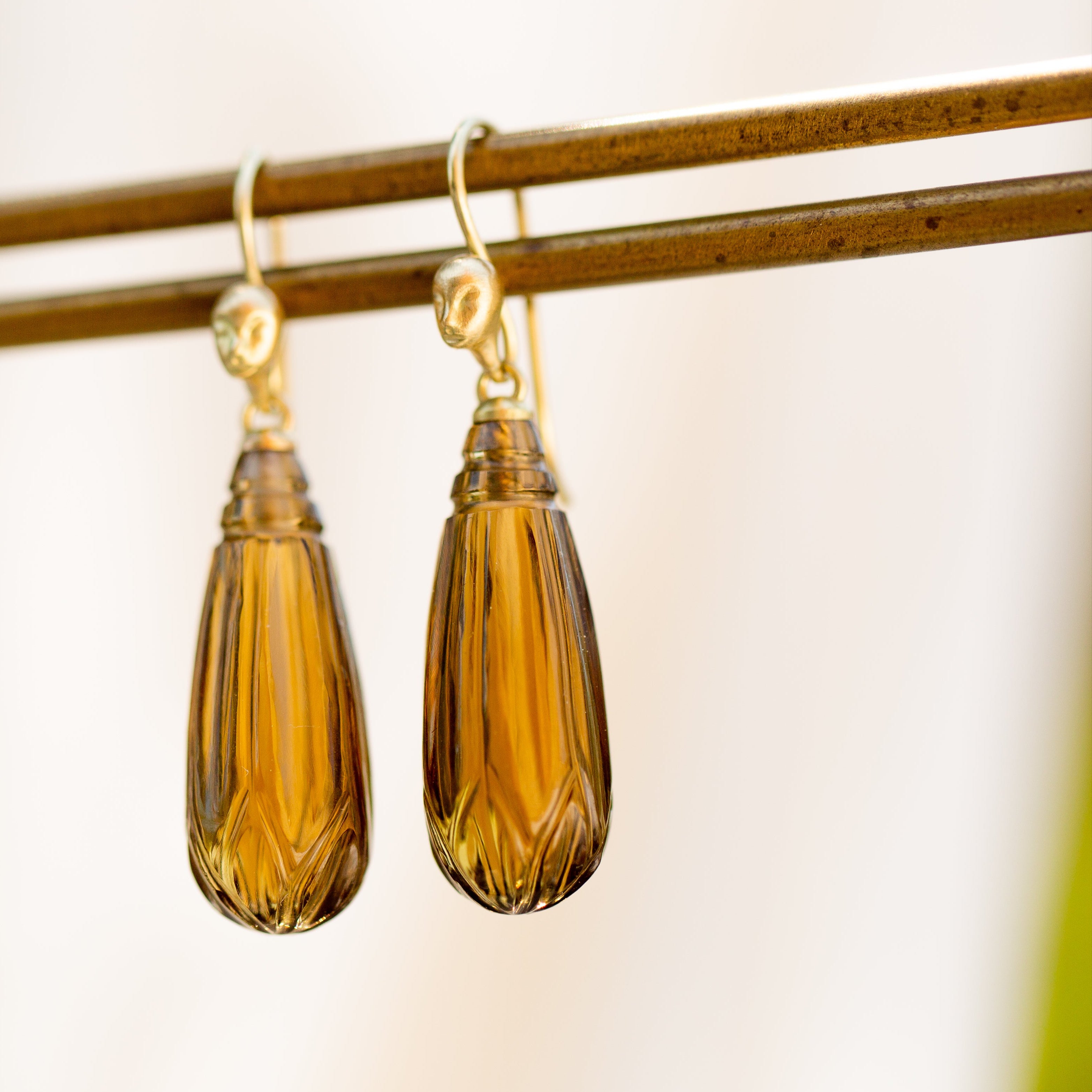 carved brown quarttz drops hang beneath gold ear wires with faces