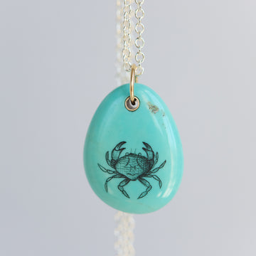 Turquoise pendant with crab design on a light gray background