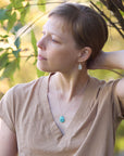 Woman with a braid wearing a turquoise necklace standing outdoors with trees in the background