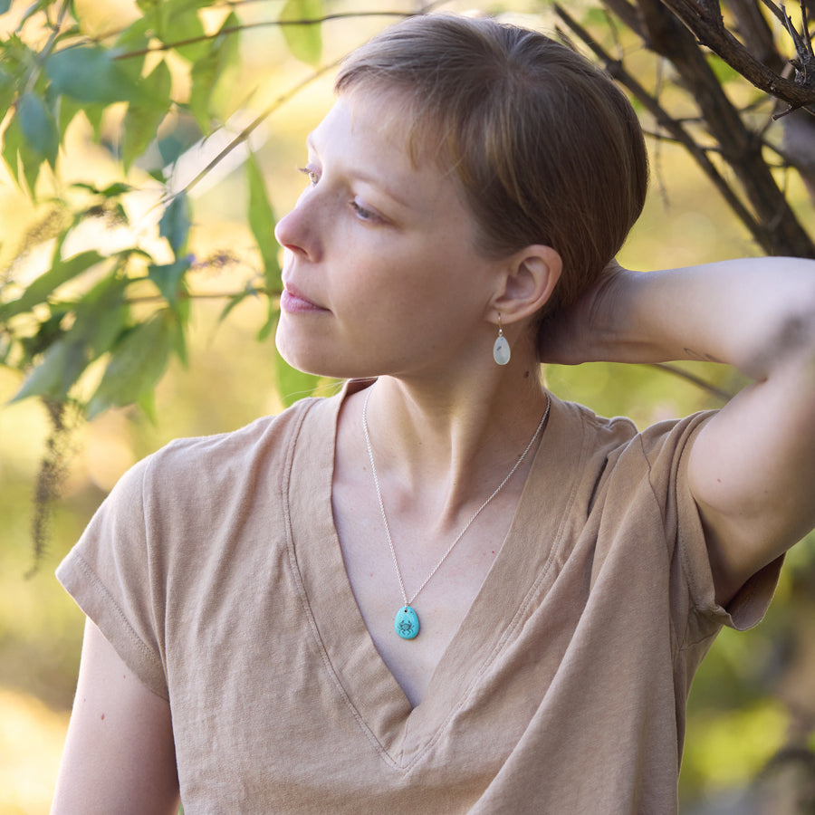 Woman with a braid wearing a turquoise necklace standing outdoors with trees in the background