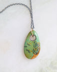 Necklace with a turquoise pendant featuring fish and seaweed illustrations on a textured surface