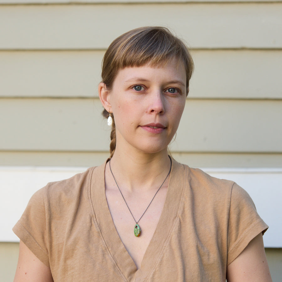 Woman with a braid wearing a beige top and necklace against a neutral background