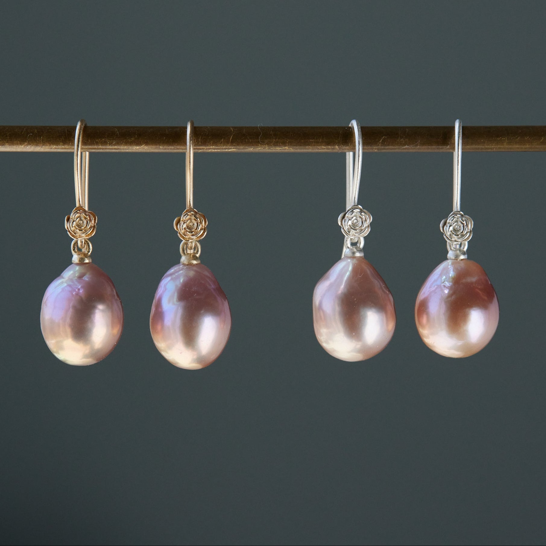 two pairs, silver and gold, pink pearl earrings with rose flower ear wires hang from a brass bar.