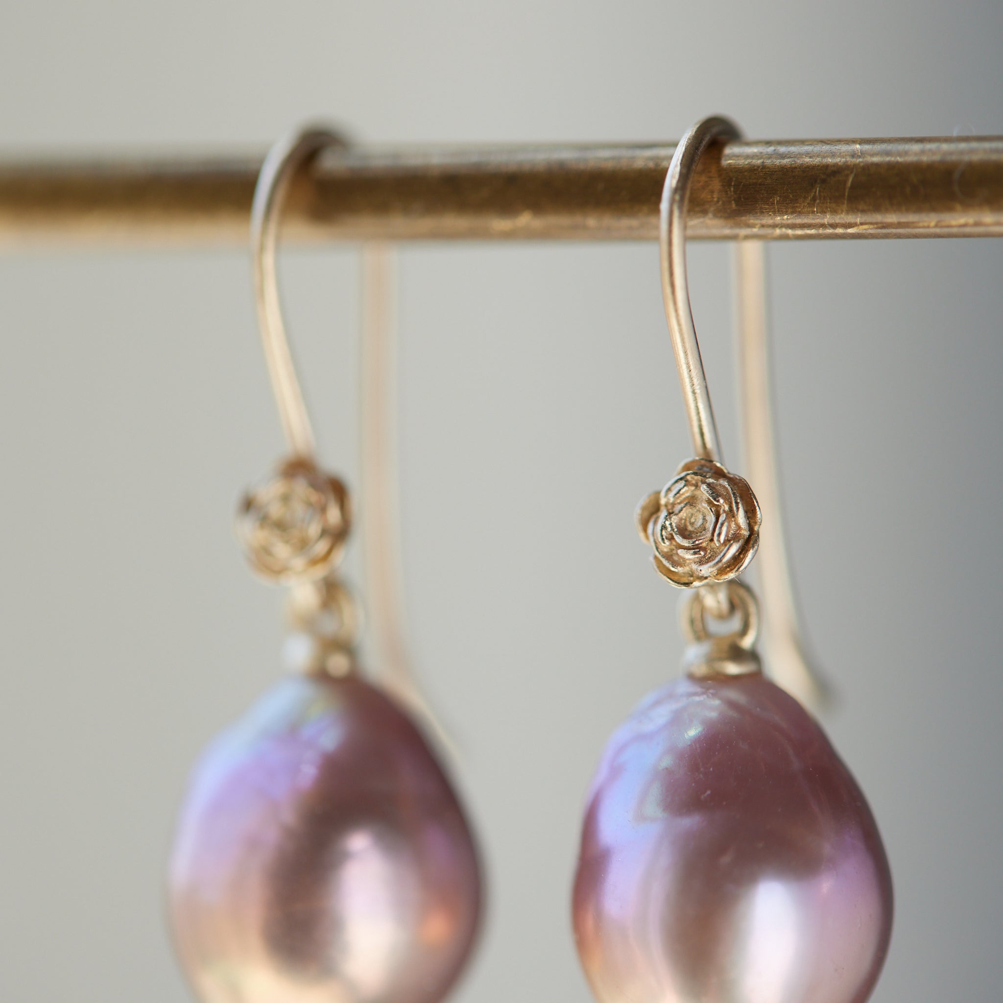 detail shot of pink pearl drop earrings with 14k yellow gold ear wires with rose accents. 
