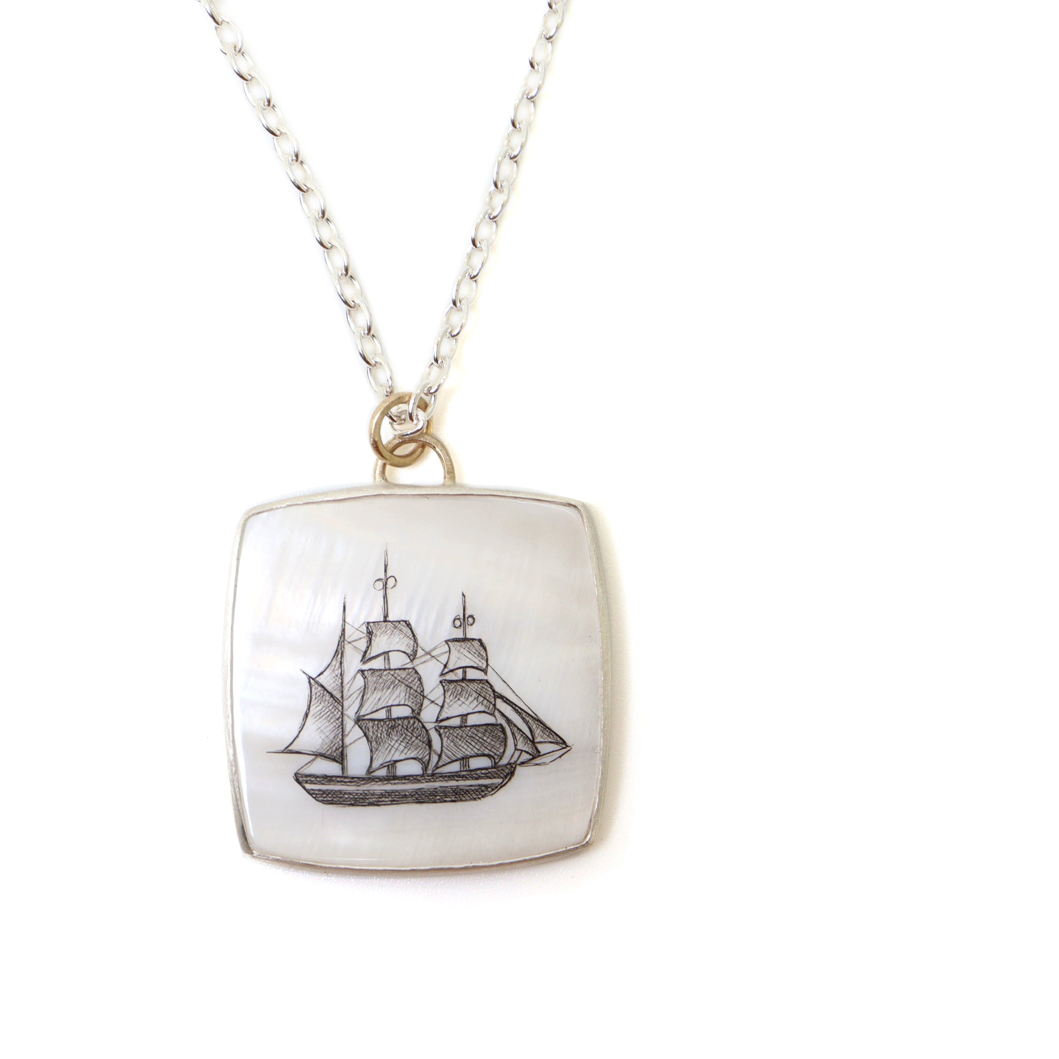a square mother of pearl slice is set in silver with a gold ring and silver chain. An old whaling ship is hand etched into the surface with black ink, called scrimshaw.