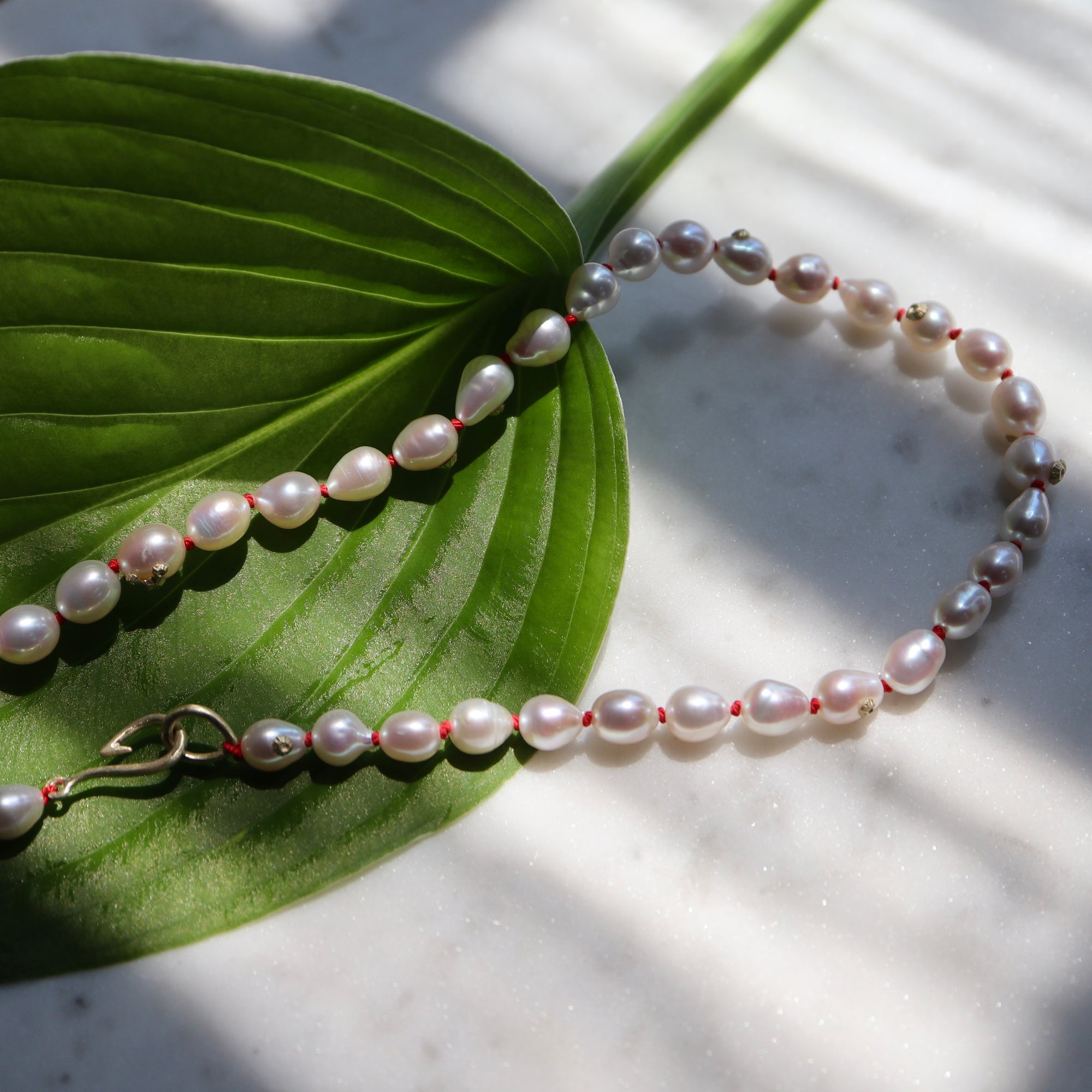 pearl strand with red knots and gold fish hook clasp. photographed on green leaf