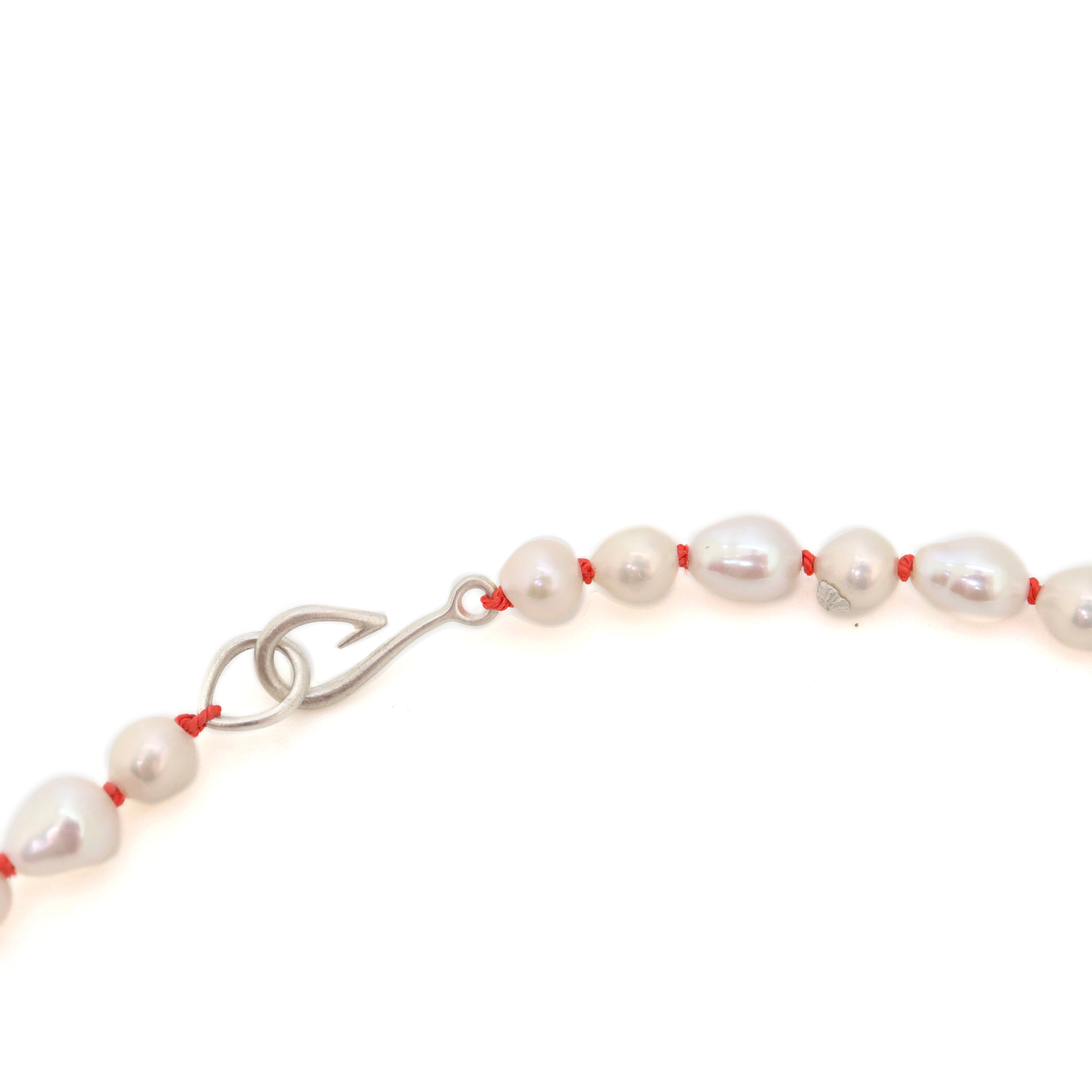 detail of necklace made of multi sized white freshwater baroque pearls strung on coral silk with silver barnacles and fish hook clasp