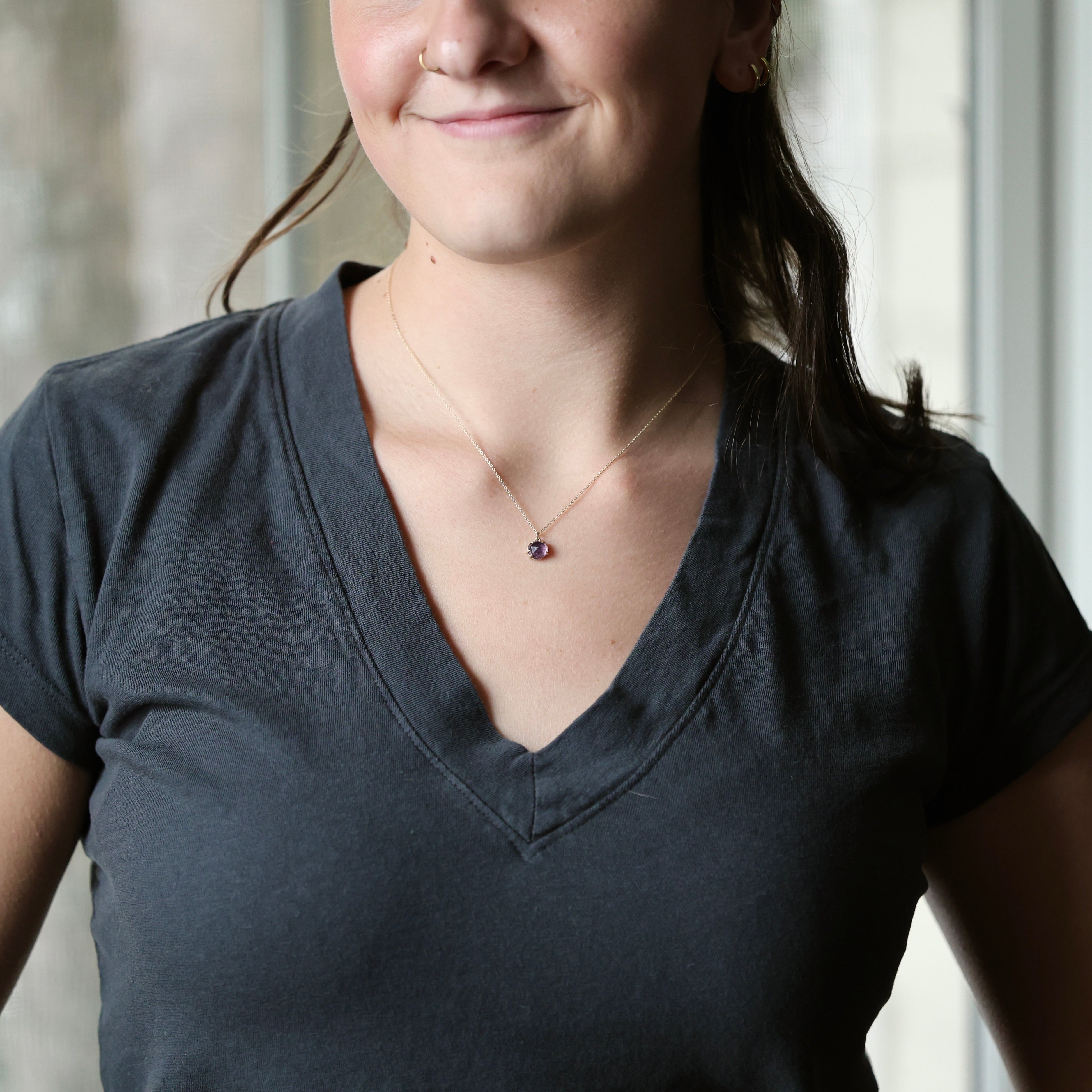 woman wearing dark grey shirt with purple pendant necklace