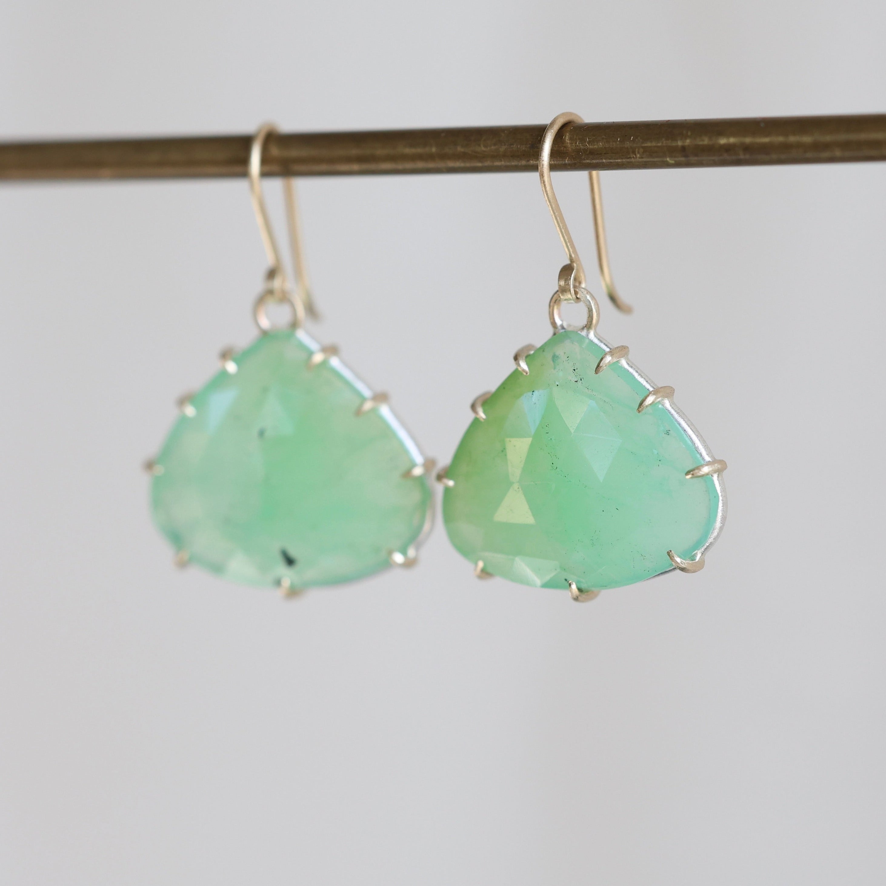 Pair of green teardrop earrings on a thin rod against a light background