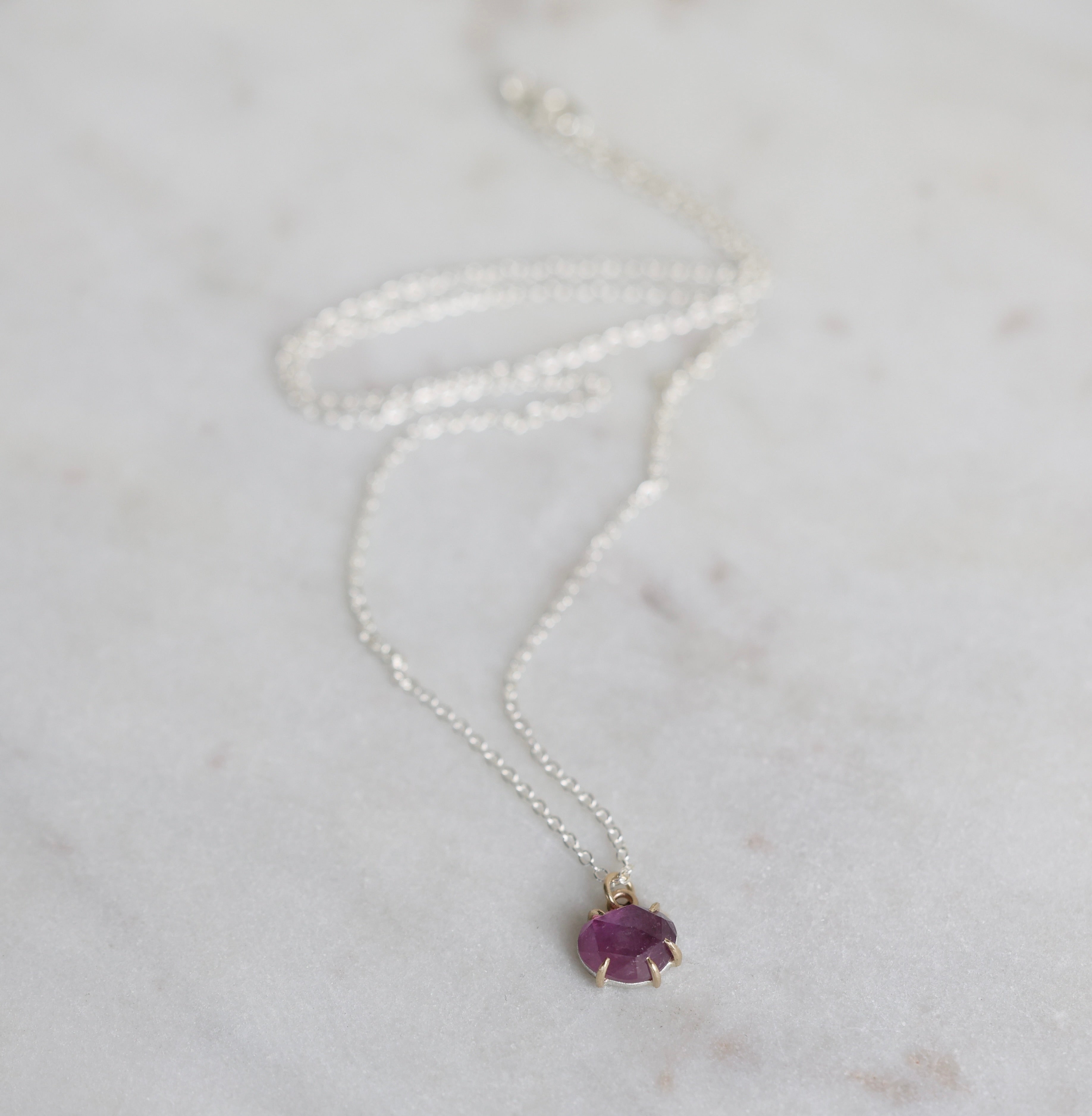 Silver necklace with a purple gemstone pendant on a light gray background