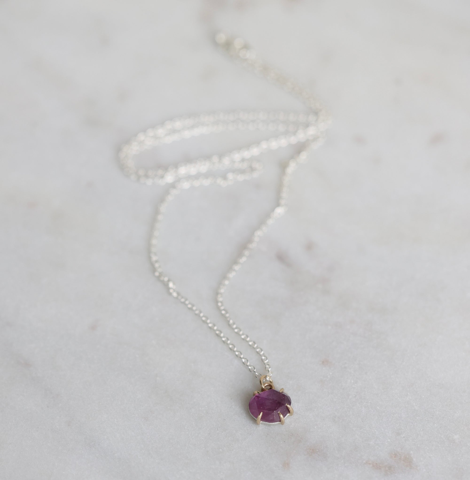 Silver necklace with a purple gemstone pendant on a light gray background