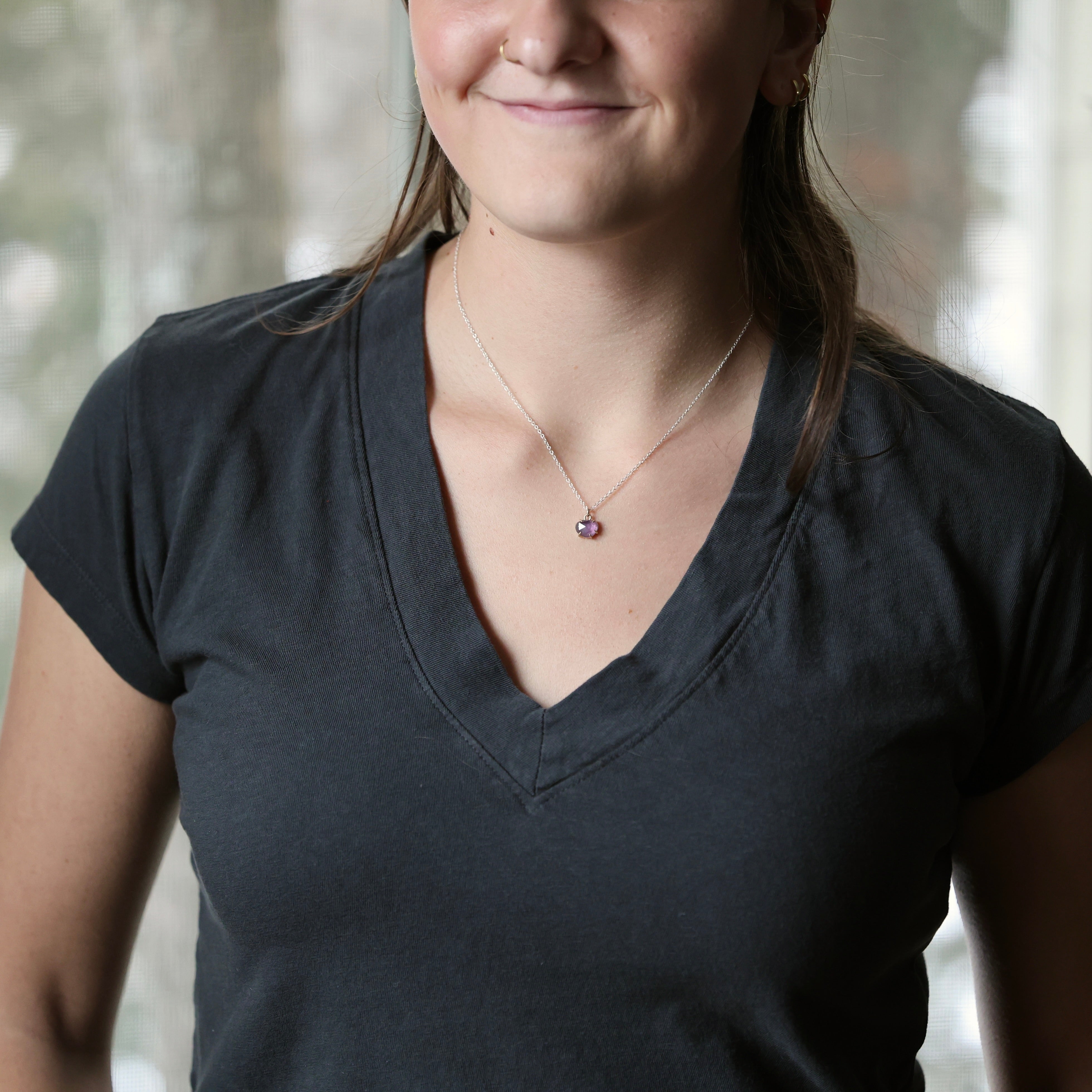 woman wearing dark grey shirt with purple pendant necklace