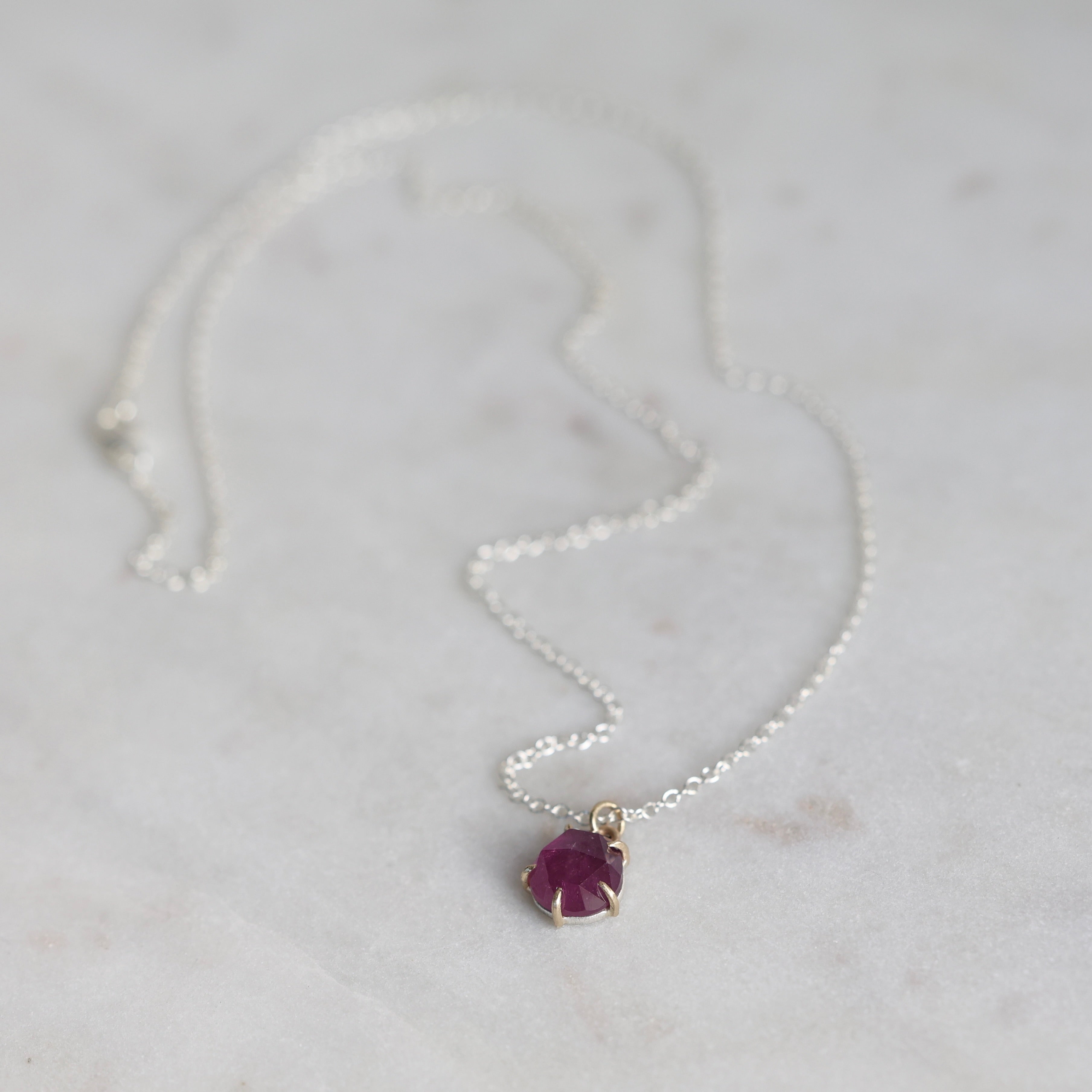 Silver necklace with a purple gemstone pendant on a light gray background