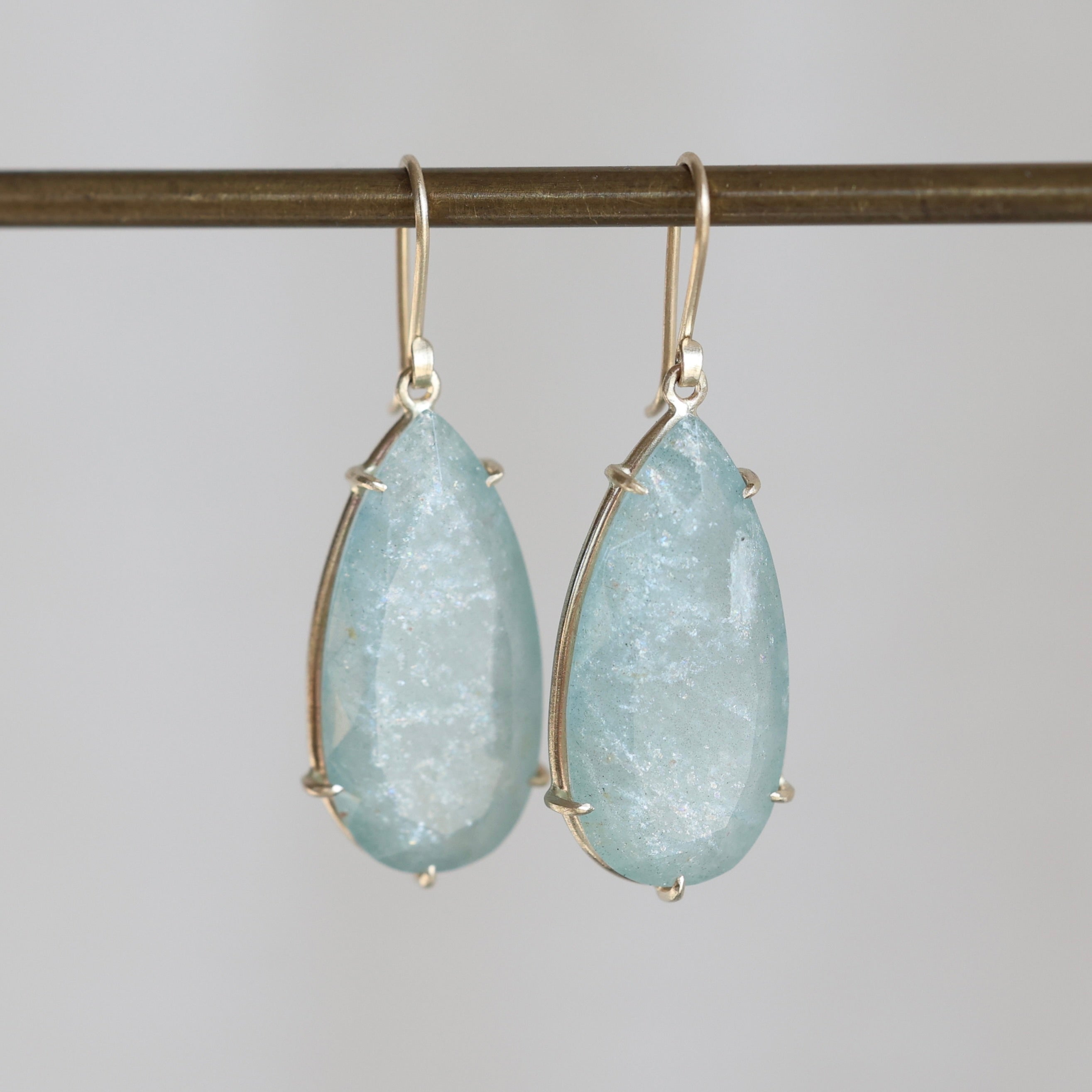Teardrop-shaped earrings with light blue gemstones on a gray background