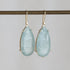 Teardrop-shaped earrings with light blue gemstones on a gray background