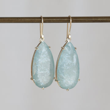 Teardrop-shaped earrings with light blue gemstones on a gray background