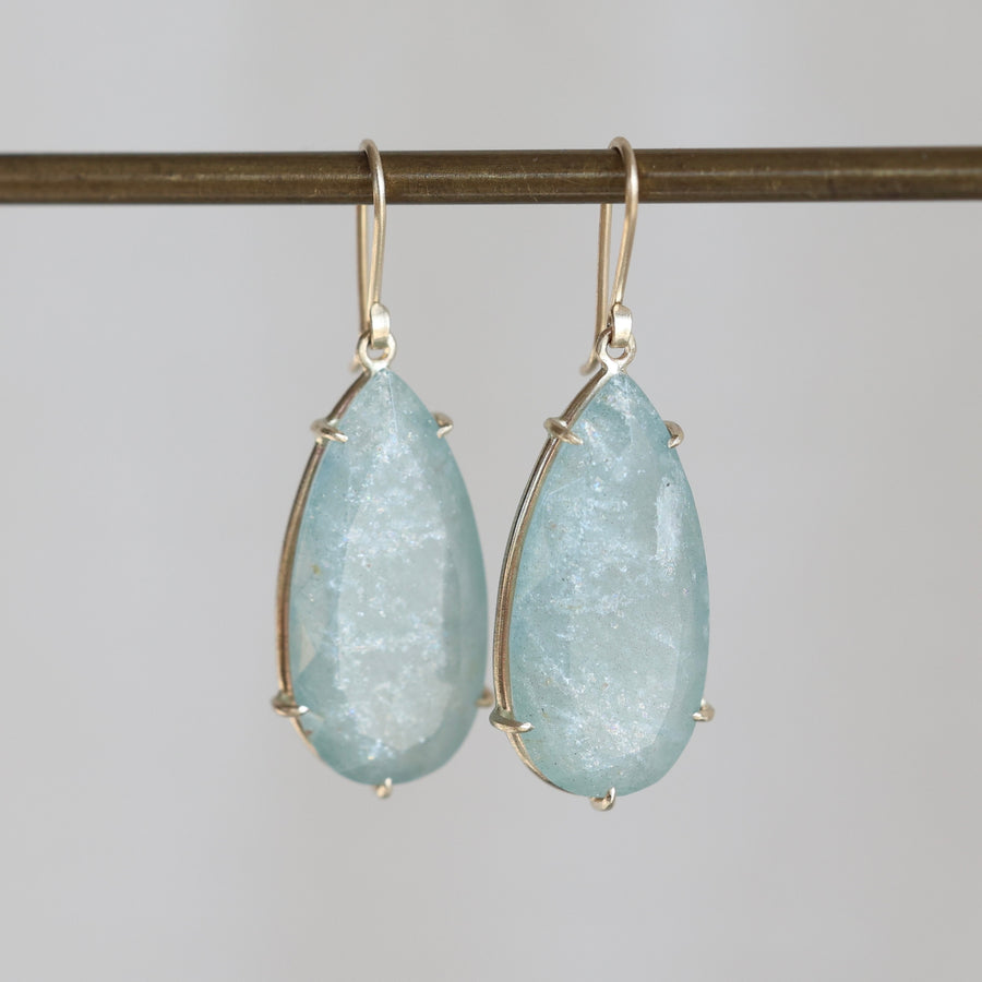 Teardrop-shaped earrings with light blue gemstones on a gray background