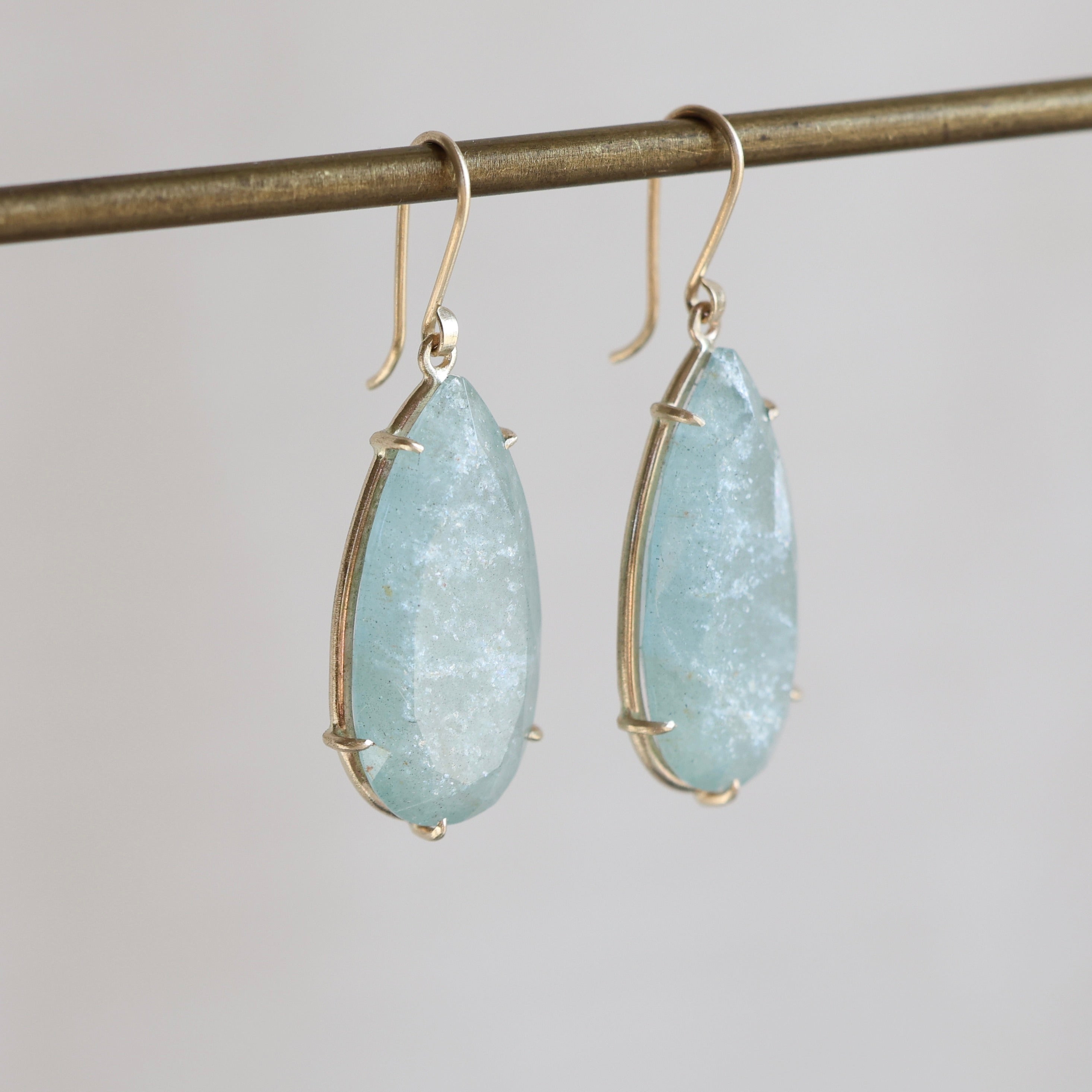 Teardrop-shaped light blue gemstone earrings on a gray background