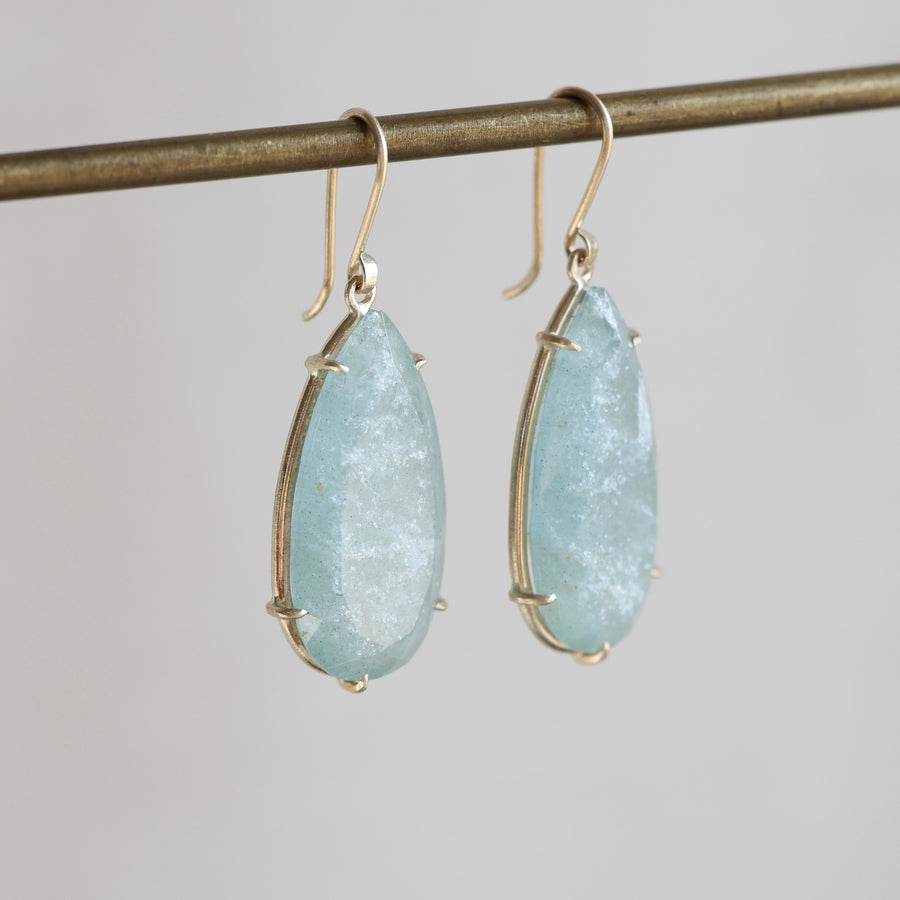 Teardrop-shaped light blue gemstone earrings on a gray background