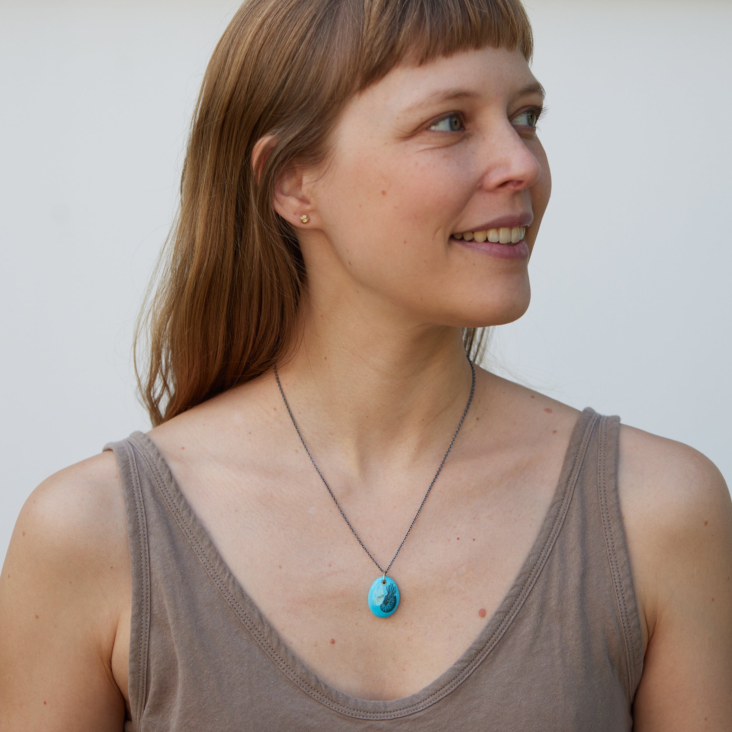 kingman turquoise pendant with inked illustration of a nautilus on oxidized silver chain with gold details