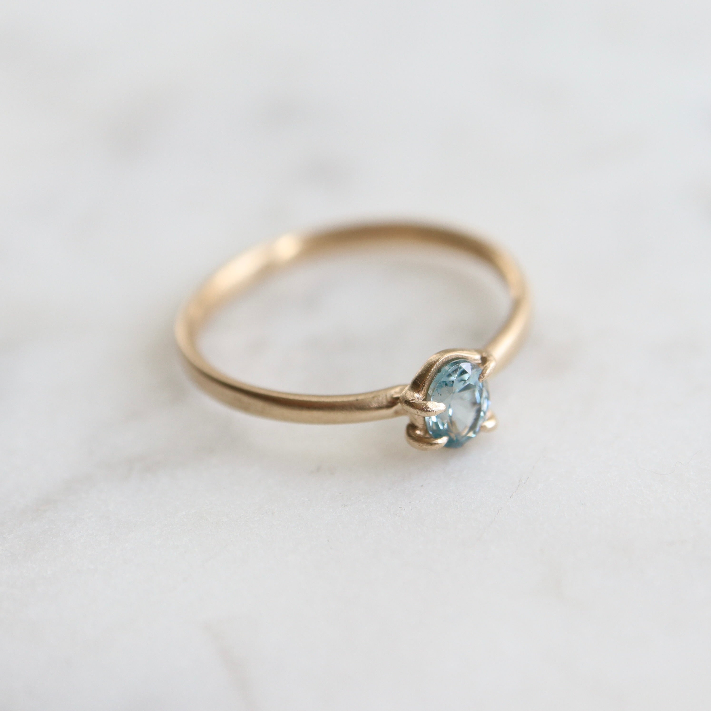 0.4ct pale blue Montana sapphire vanity ring set in 14k yellow gold with four asymmetrical prongs.