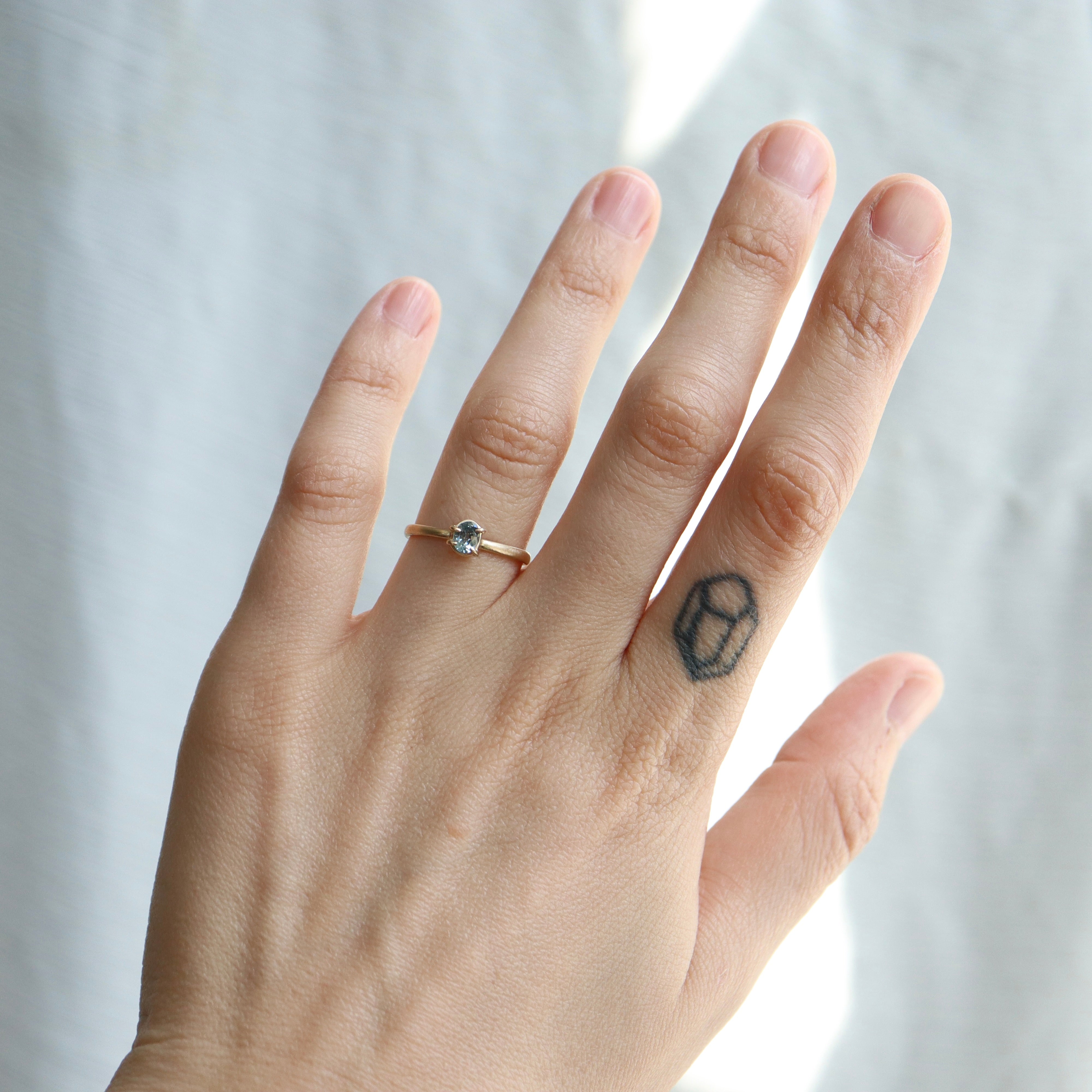 0.4ct pale blue Montana sapphire vanity ring set in 14k yellow gold with four asymmetrical prongs, displayed on a hand.