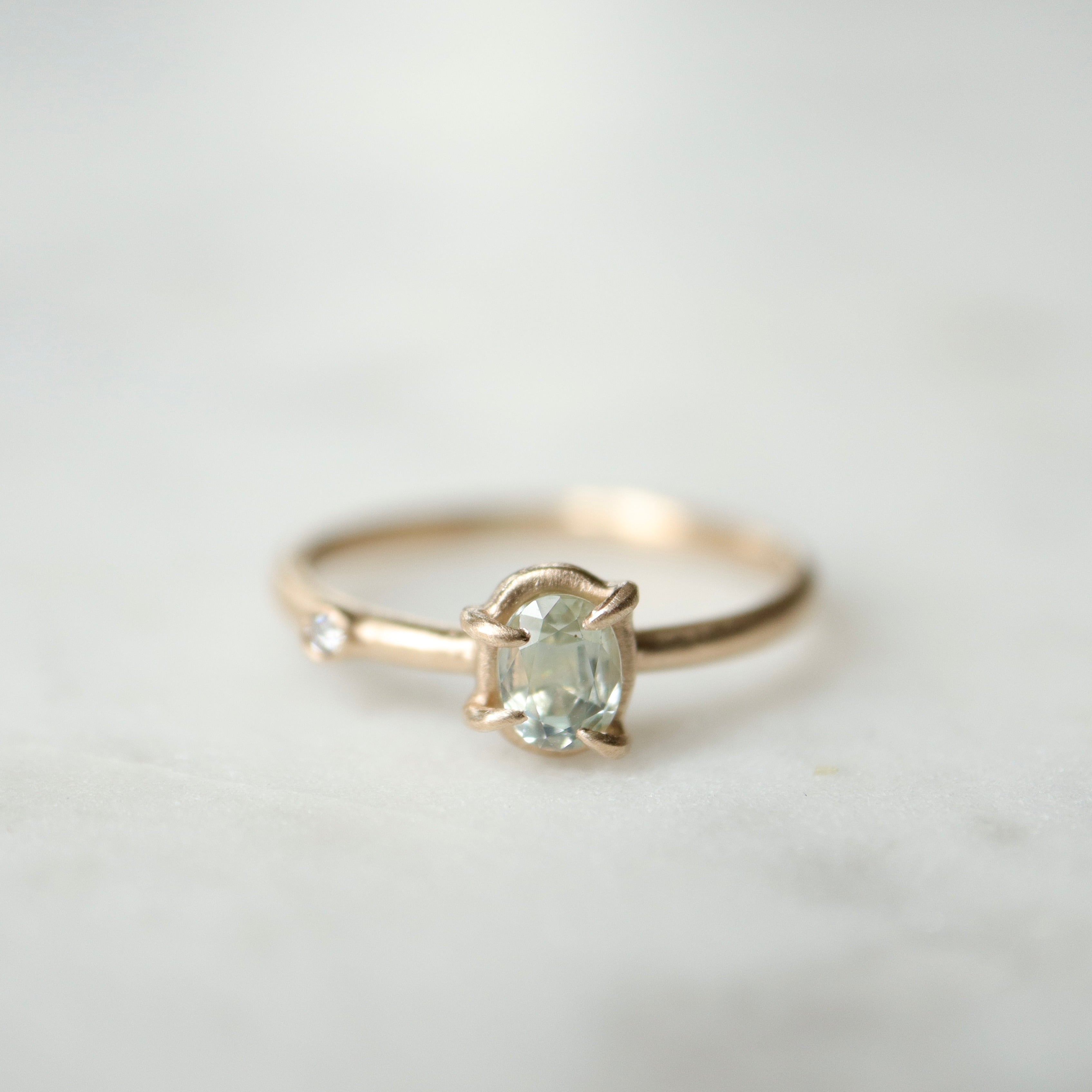 milky clean montana sapphire oval set in a gold ring via a-symetrical prongs and a single diamond accent off-set on the band.