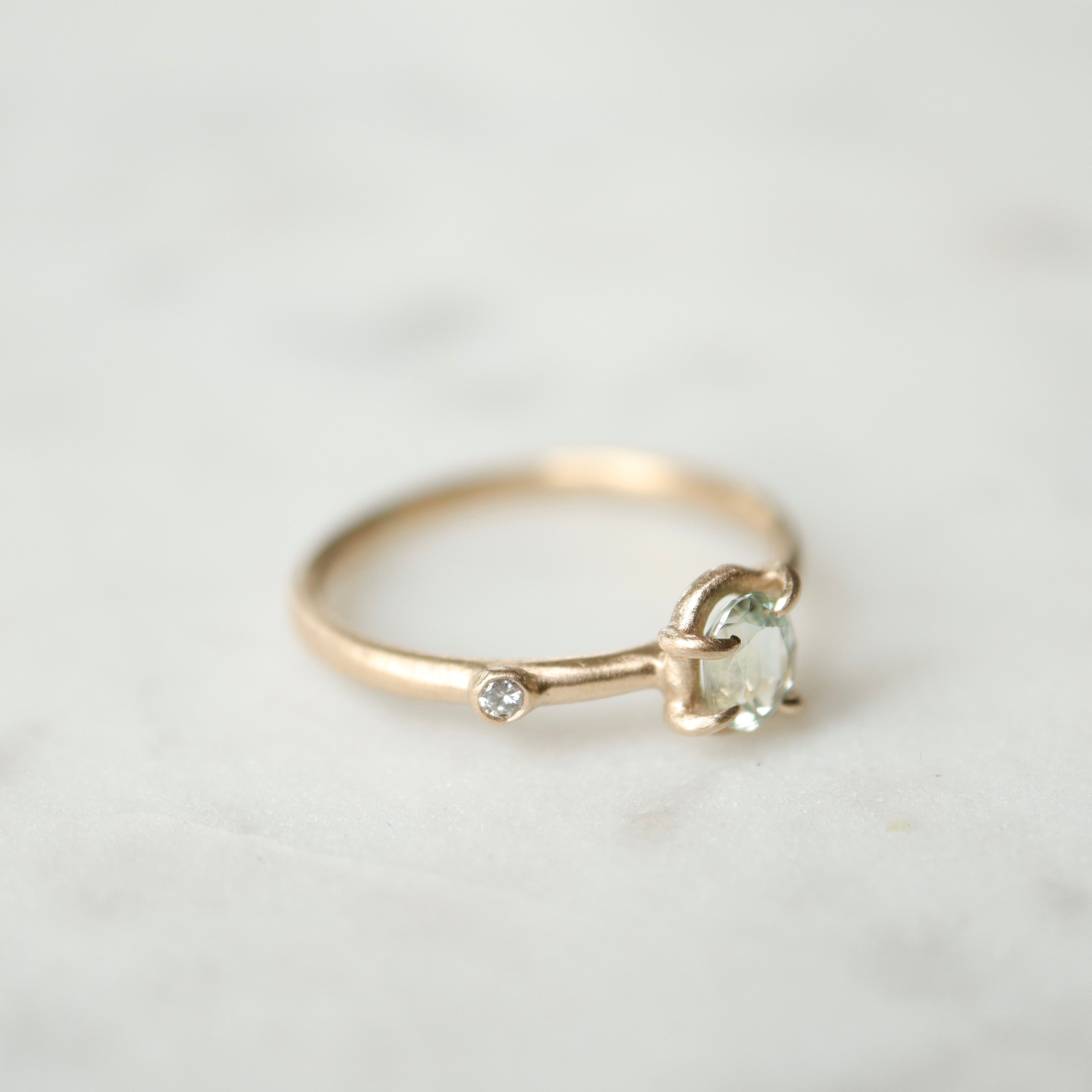 side view of milky clean montana sapphire oval set in a gold ring via a-symetrical prongs and a single diamond accent off-set on the band.