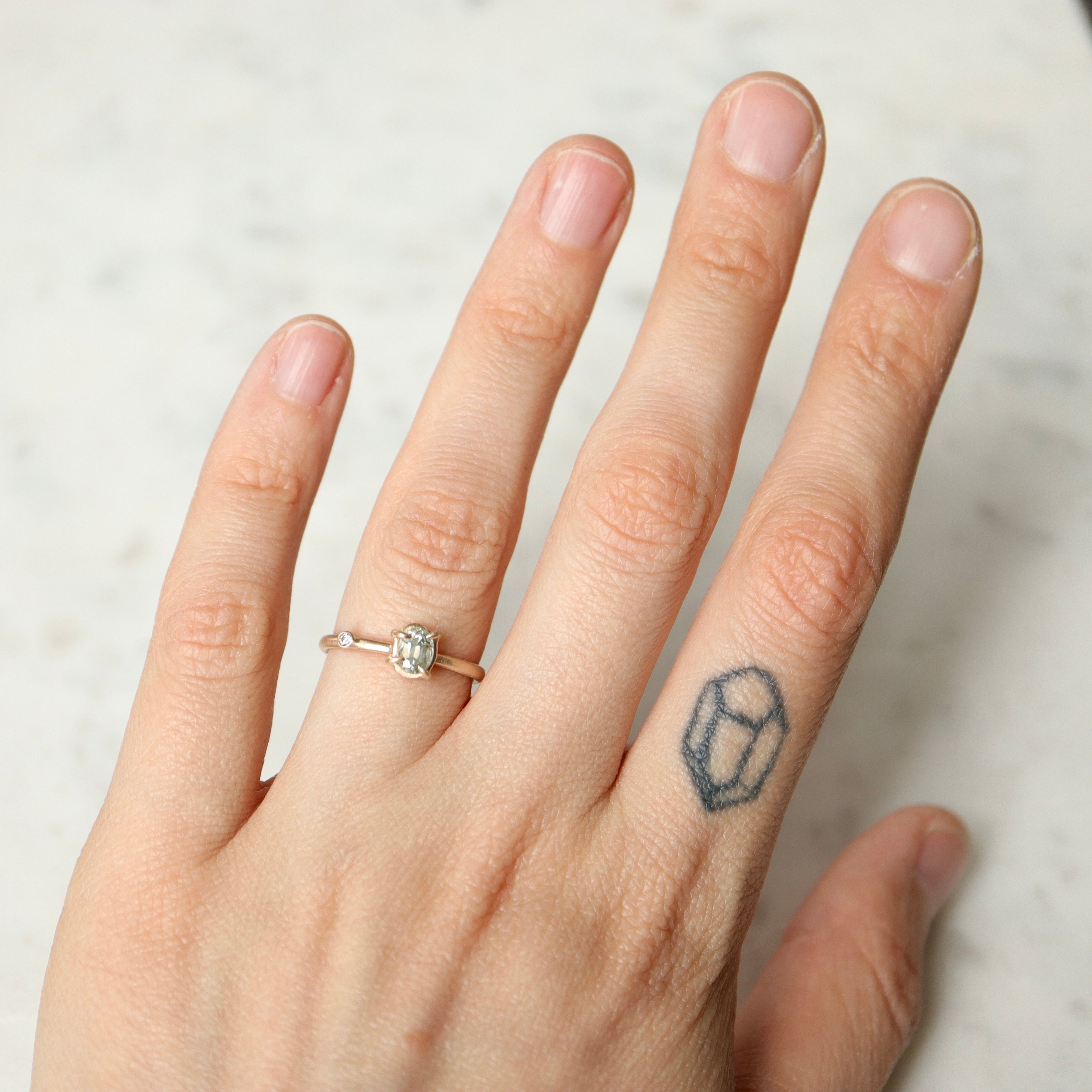 milky clean montana sapphire oval set in a gold ring via a-symetrical prongs and a single diamond accent off-set on the band- shown on hand.