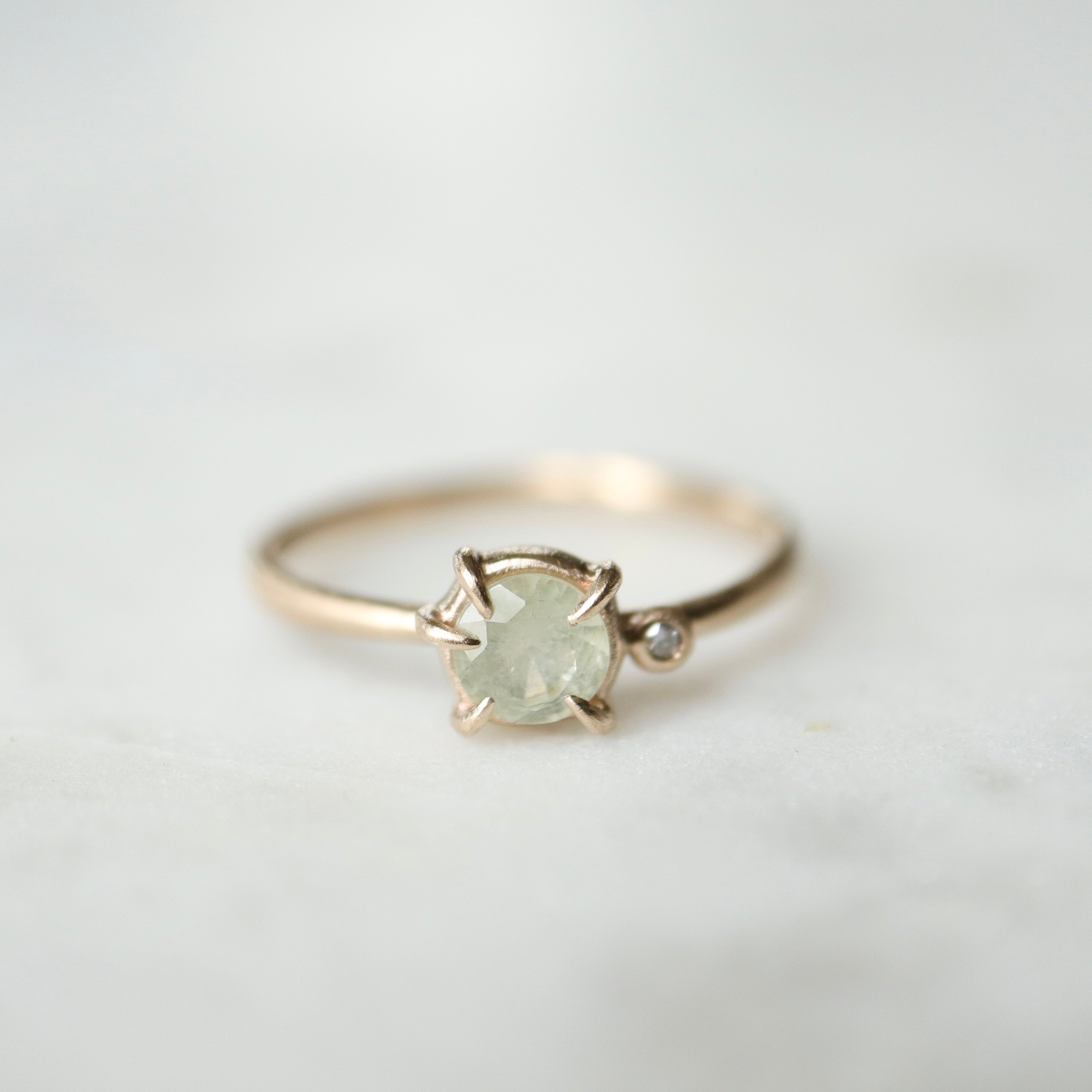 white sapphire set in a gold ring with a single white diamond on the side