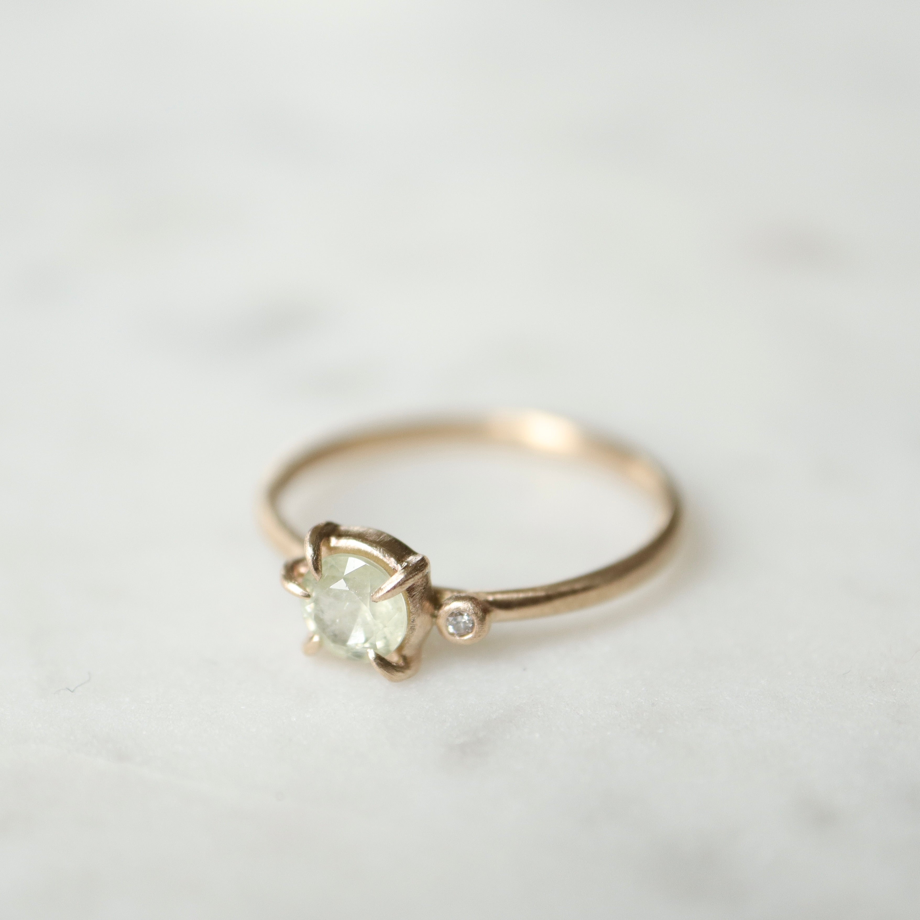 side view white sapphire set in a gold ring with a single white diamond on the side